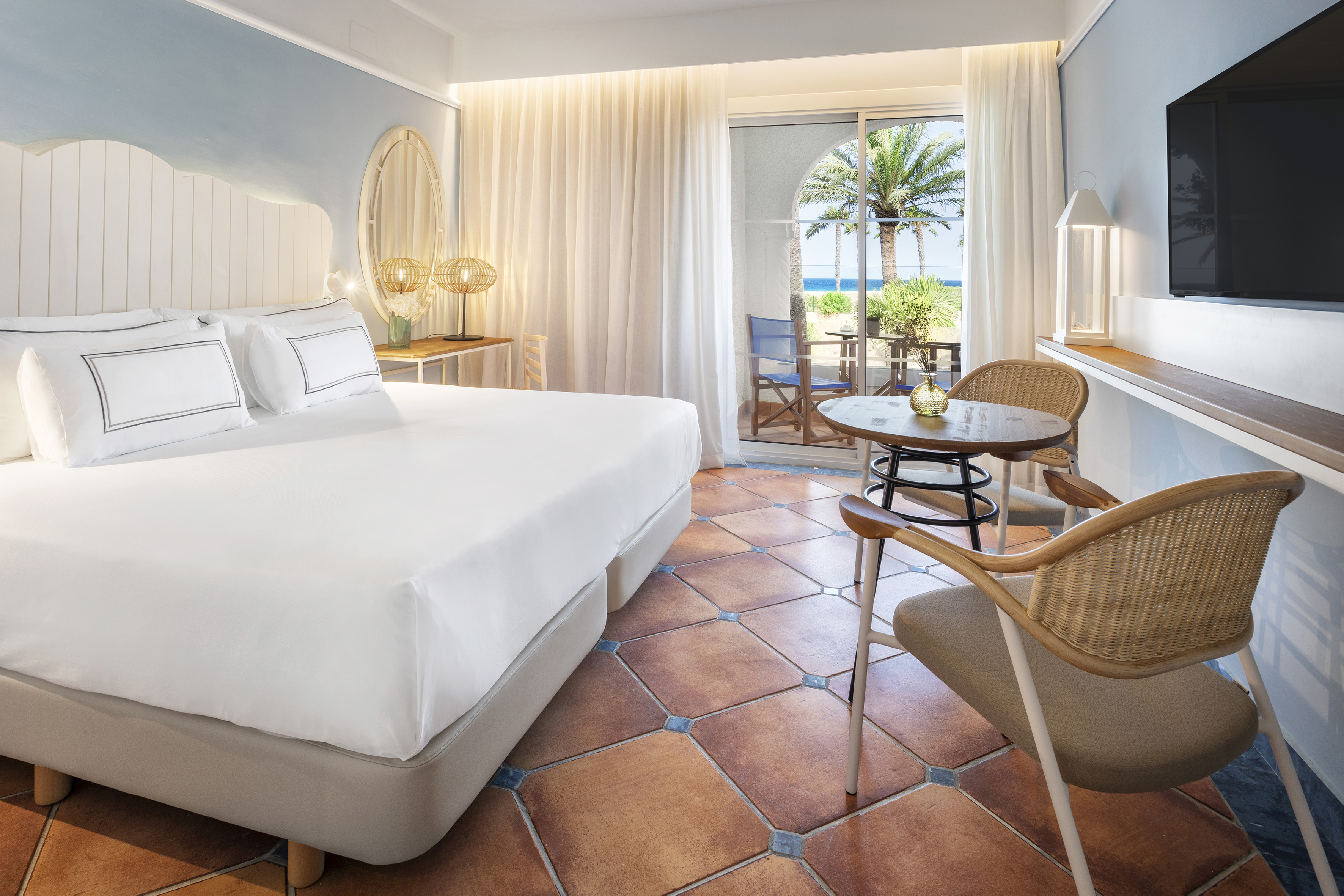Beachfront hotel room with ocean view, white bed, terracotta floor, and balcony.
