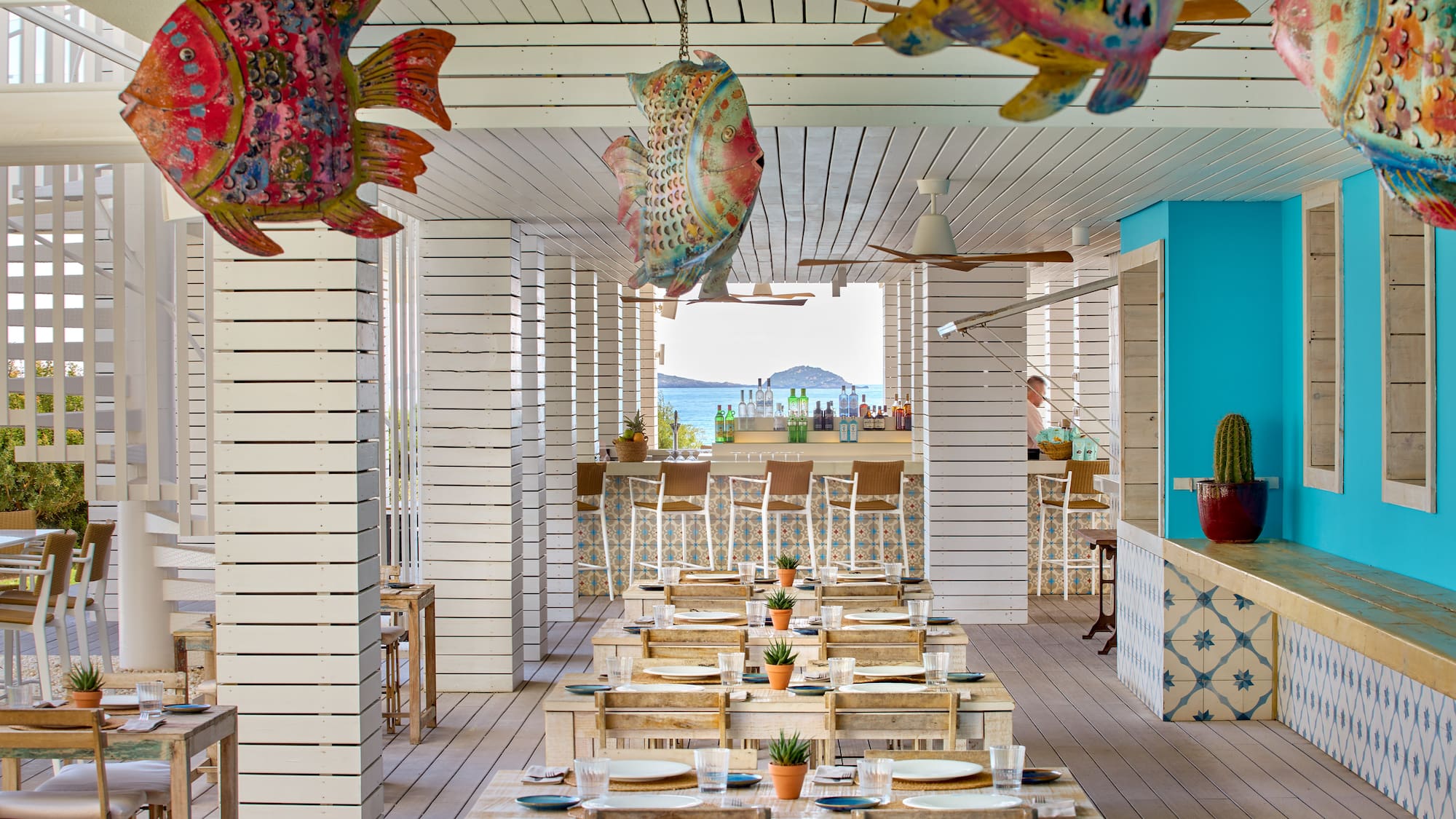 Beachfront restaurant with colorful fish decor, wooden tables, and ocean view.