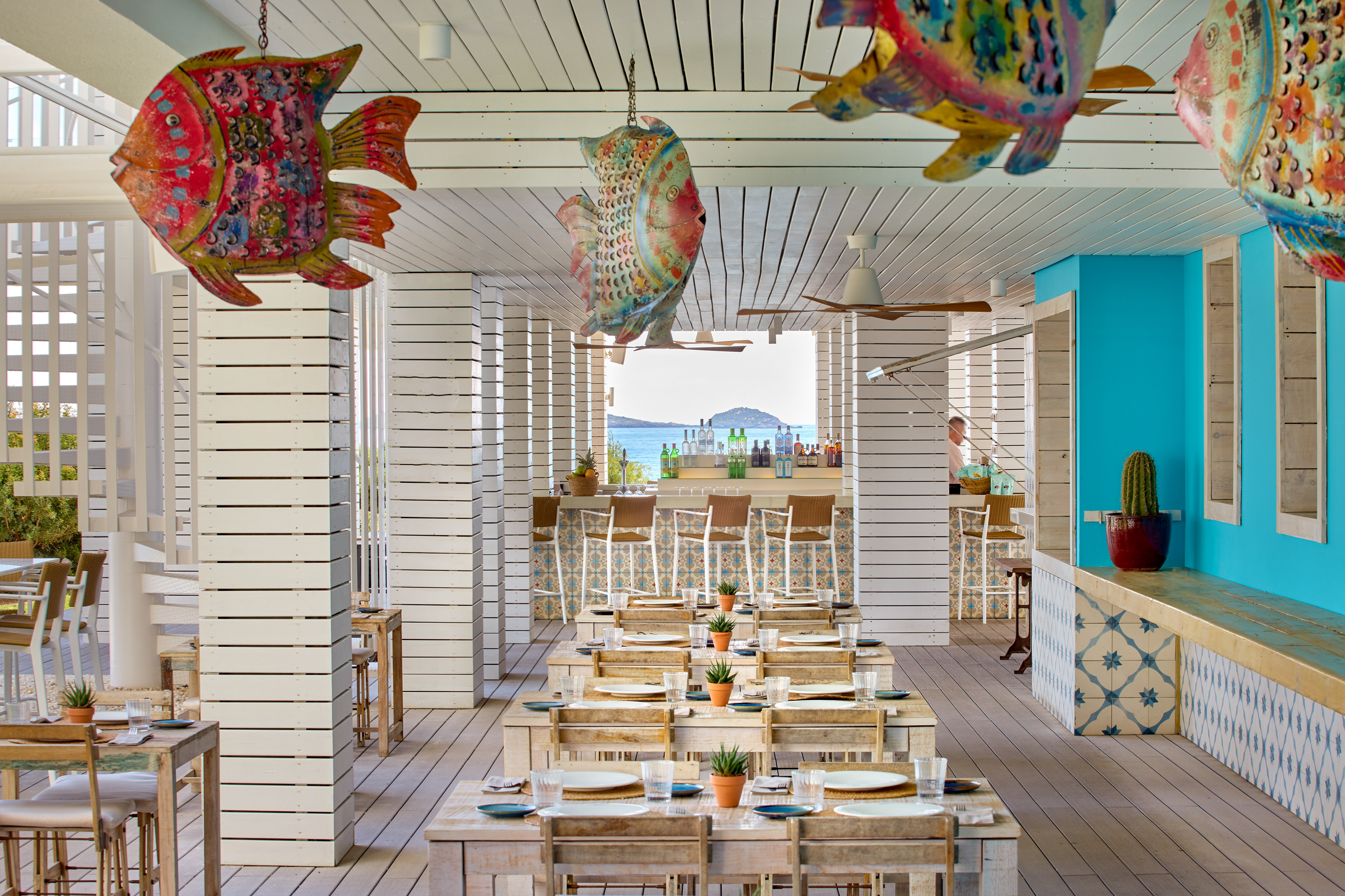 Beachfront restaurant with colorful fish decor, wooden tables, and ocean view.