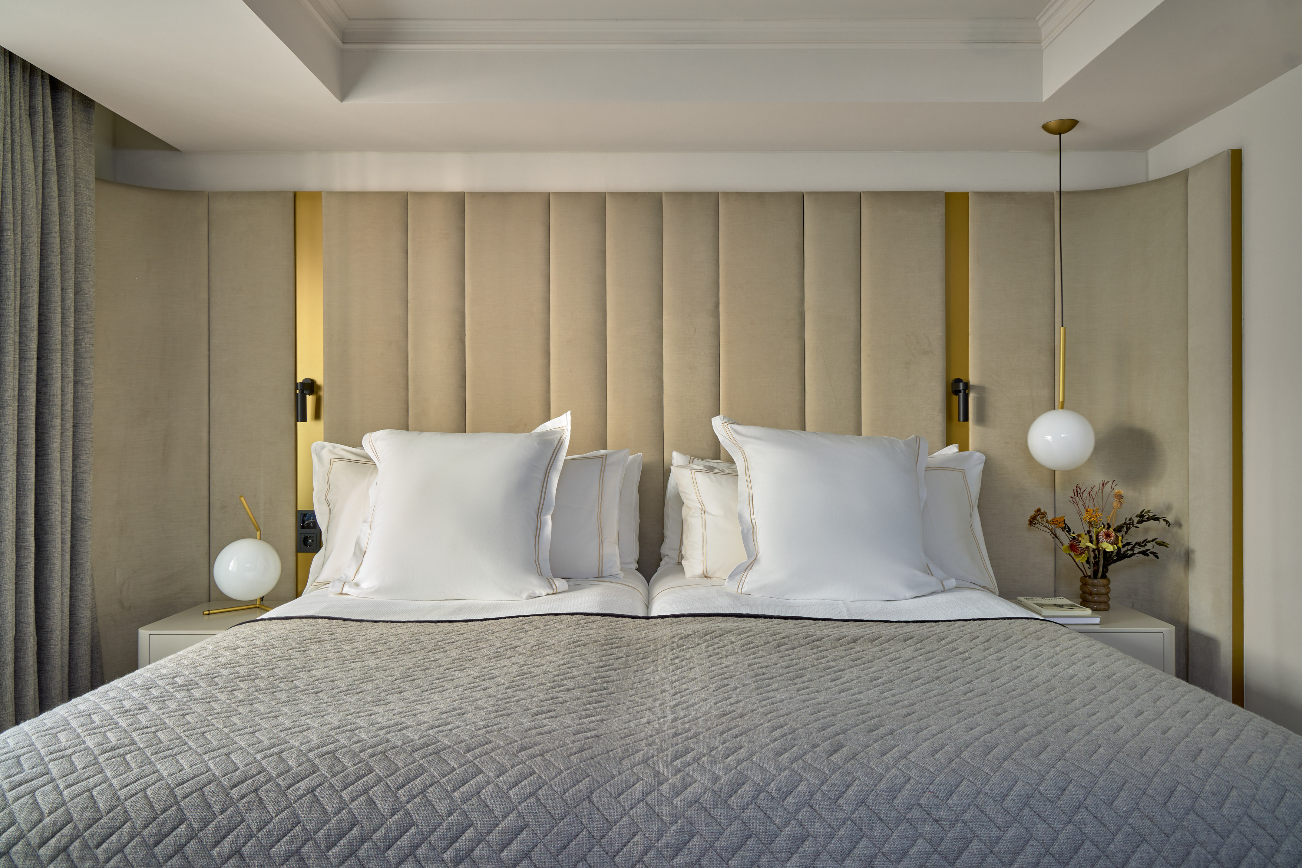 Modern bed with beige upholstered headboard, gold details, and grey quilted bedding.