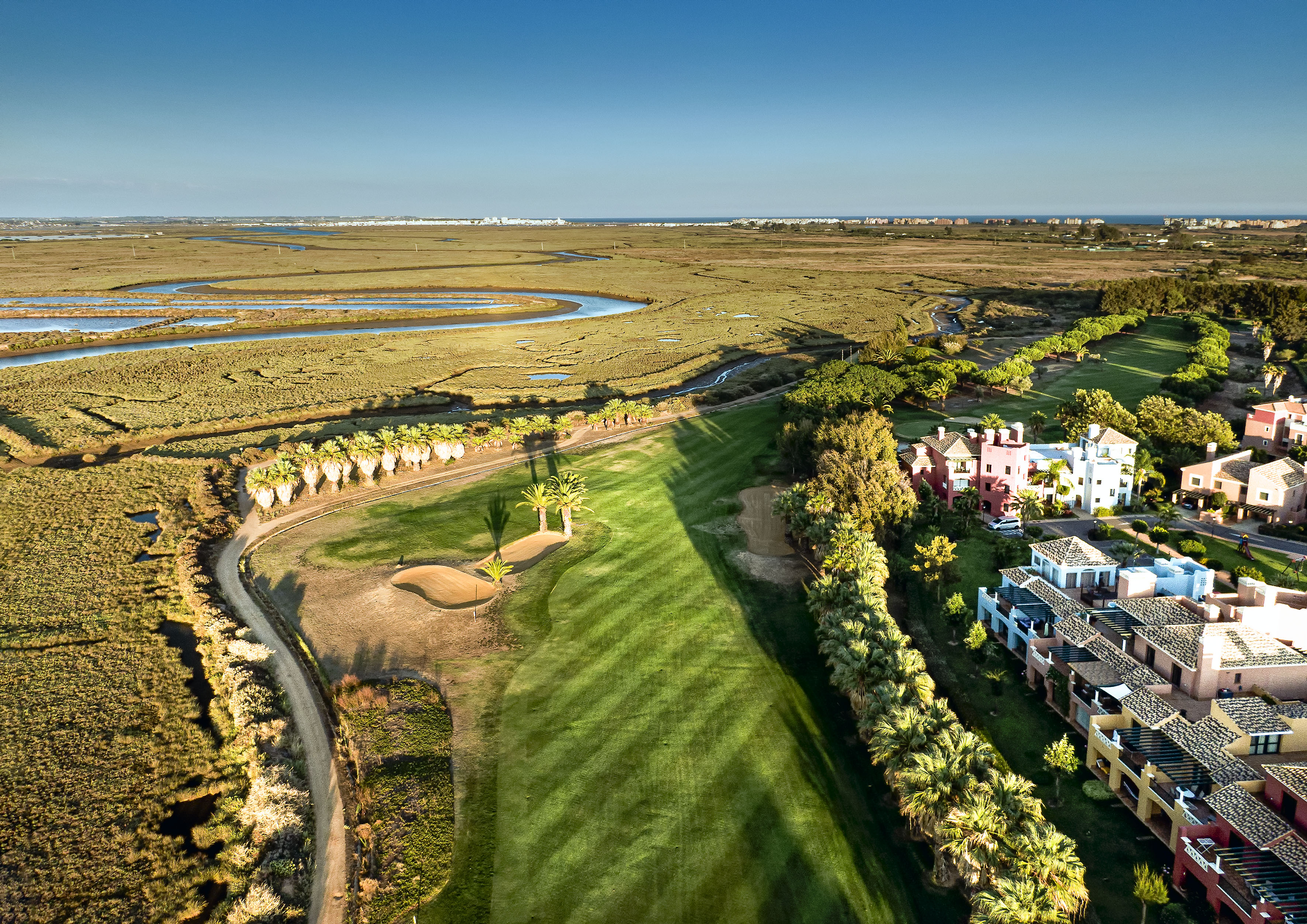 Coastal golf course with Mediterranean homes bordering expansive wetlands.