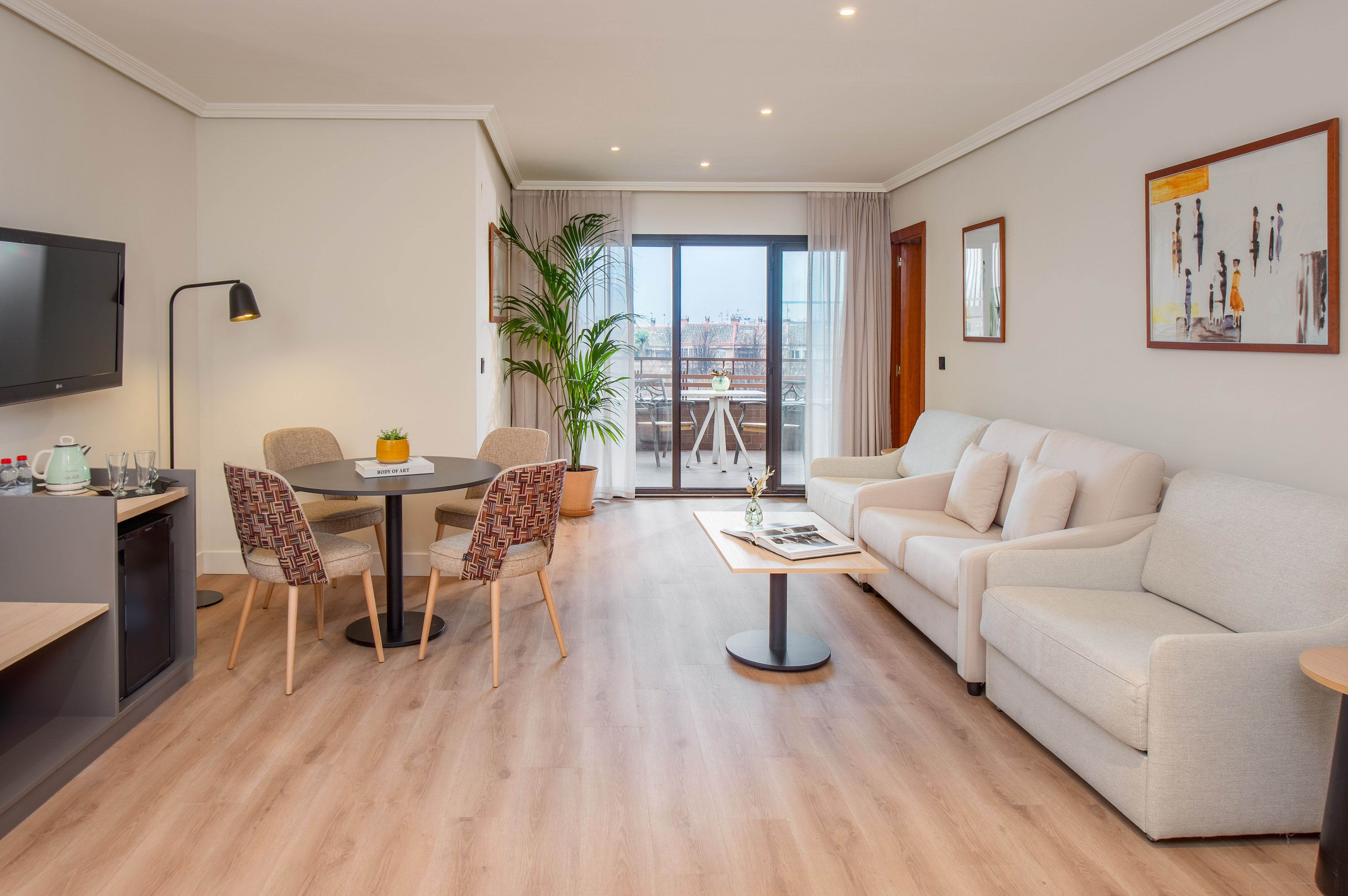 Spacious hotel suite living room with dining area, sofa, and balcony.