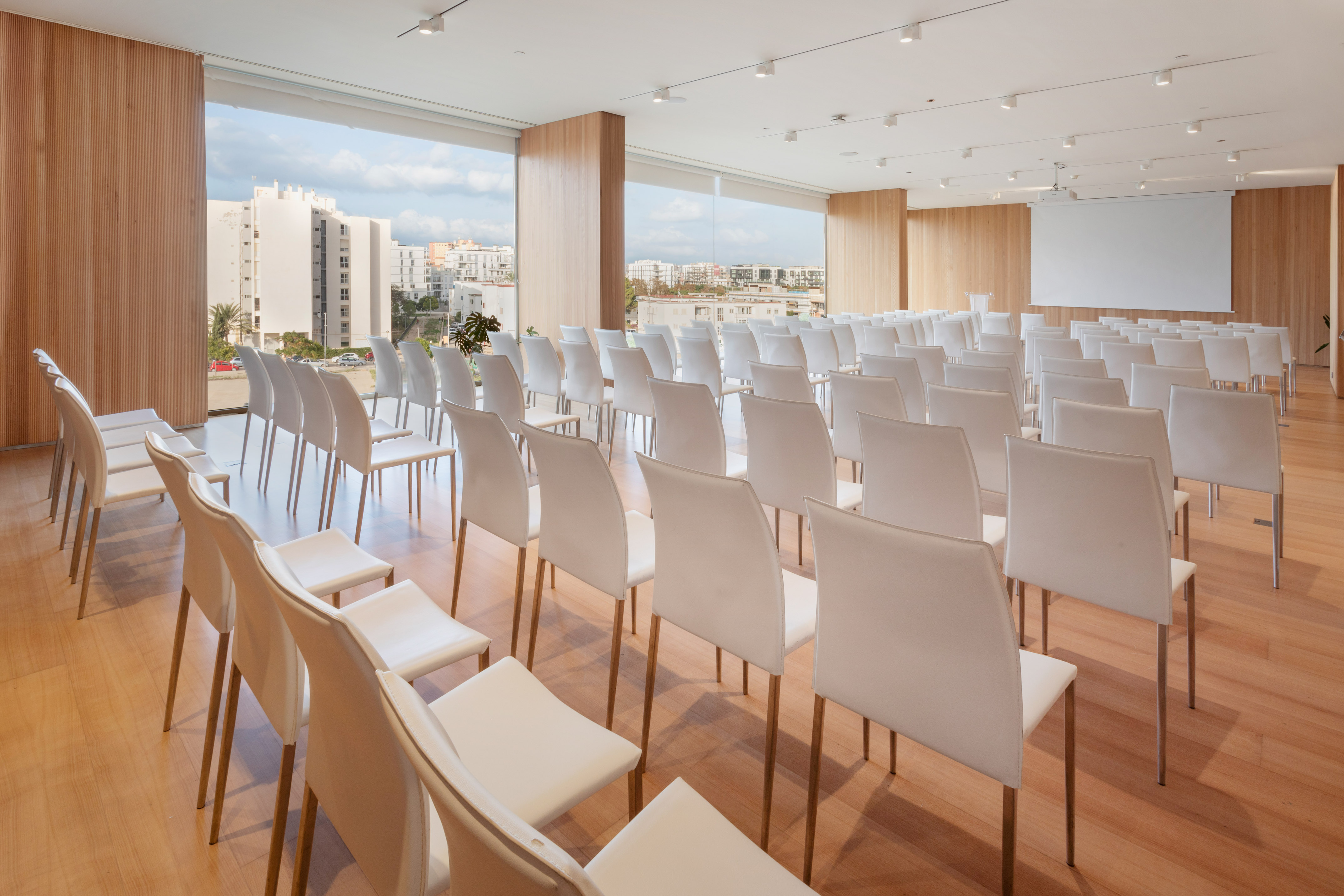 Modern conference room with white chairs, city view, and projector screen.