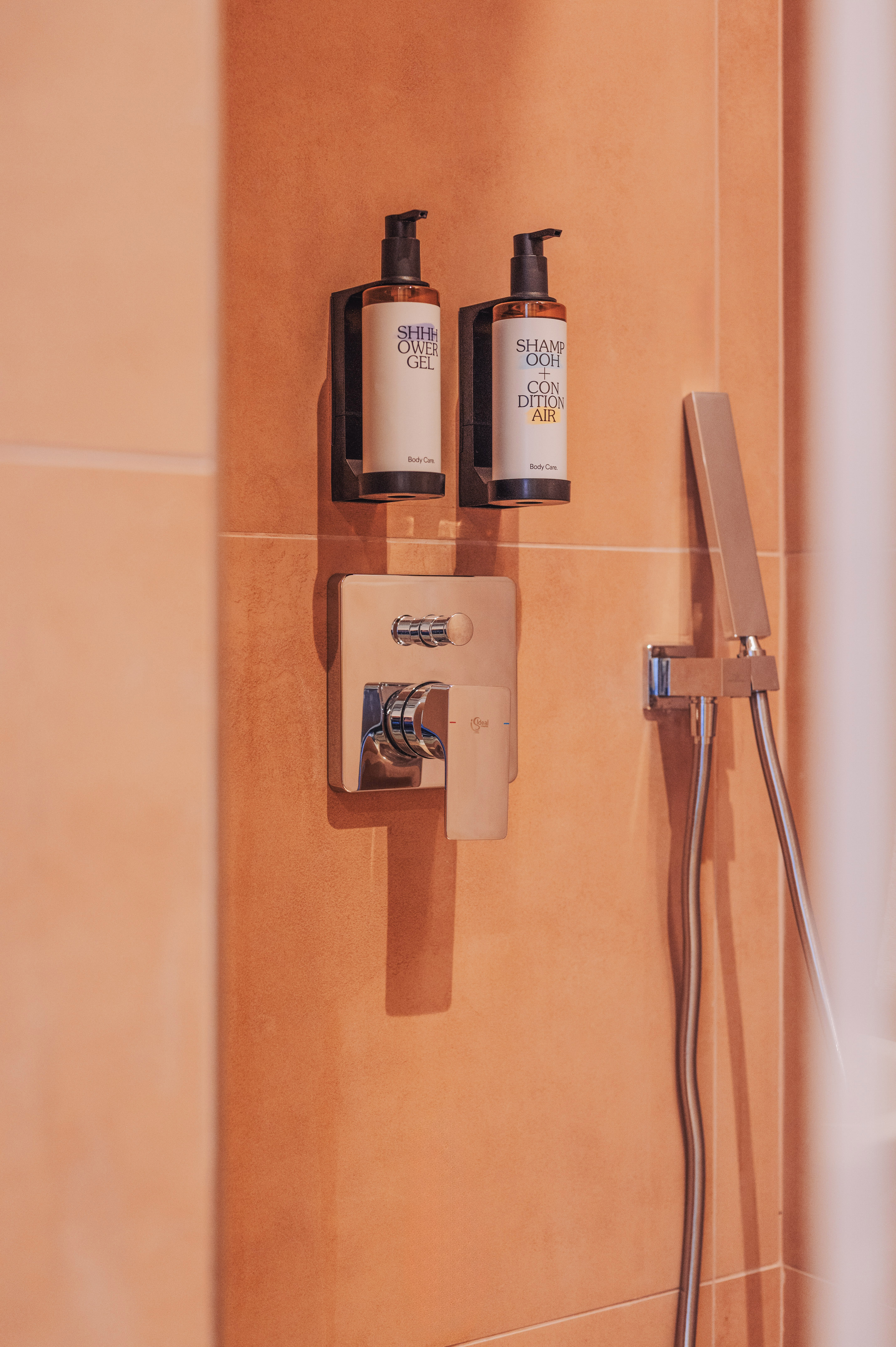 Modern shower with wall-mounted shampoo, conditioner, and shower gel dispensers.