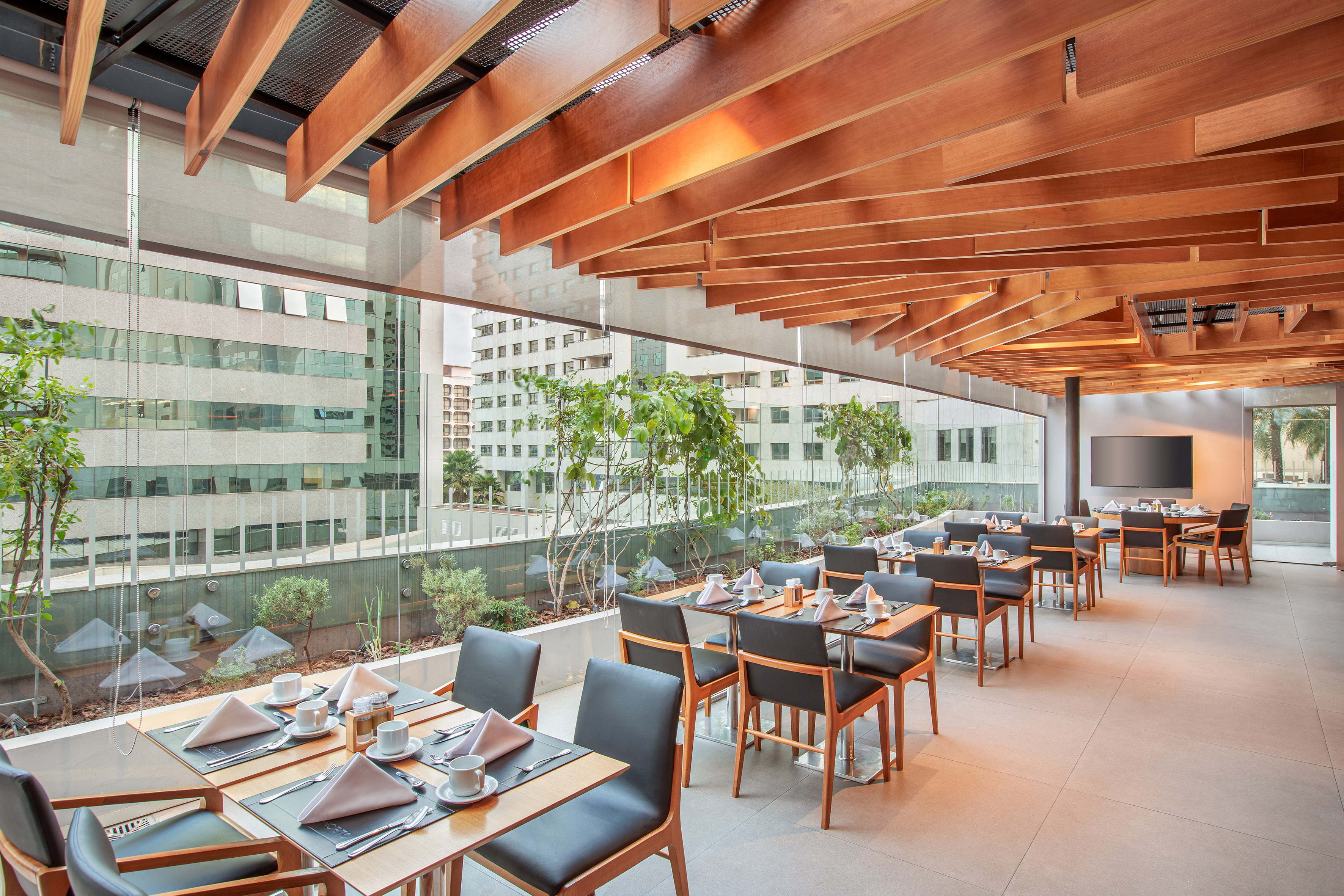 Modern restaurant with city view, wood slatted ceiling, and set dining tables.