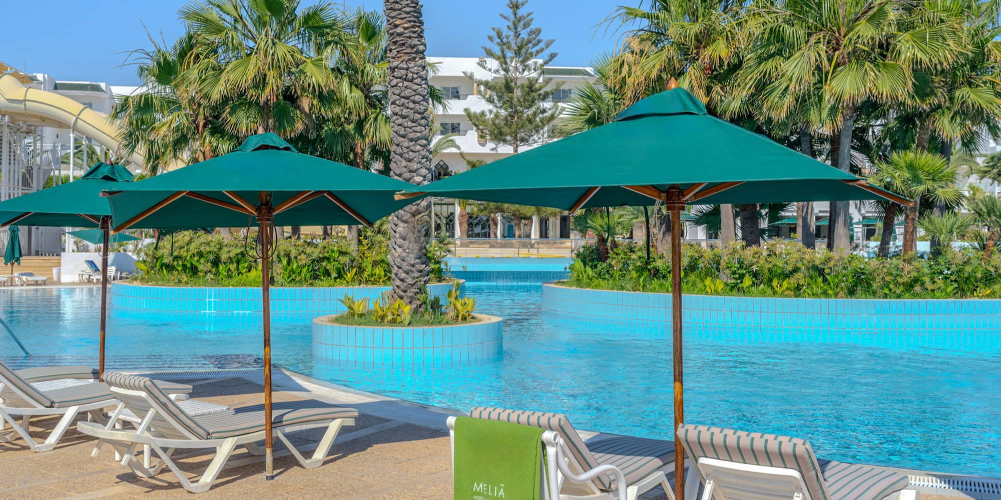 Meliá resort pool with lounge chairs, green umbrellas, and palm trees.