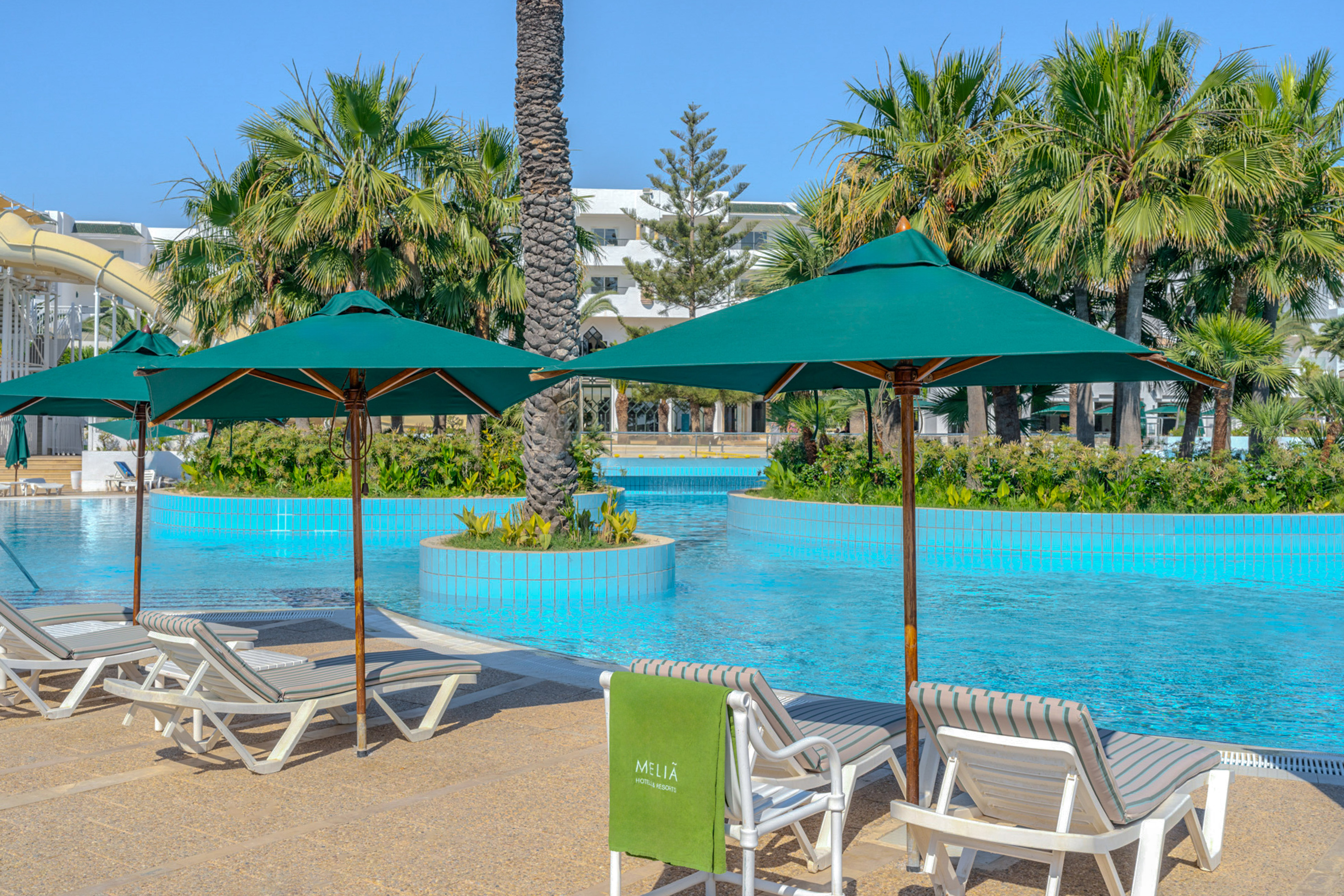 Meliá resort pool with lounge chairs, green umbrellas, and palm trees.