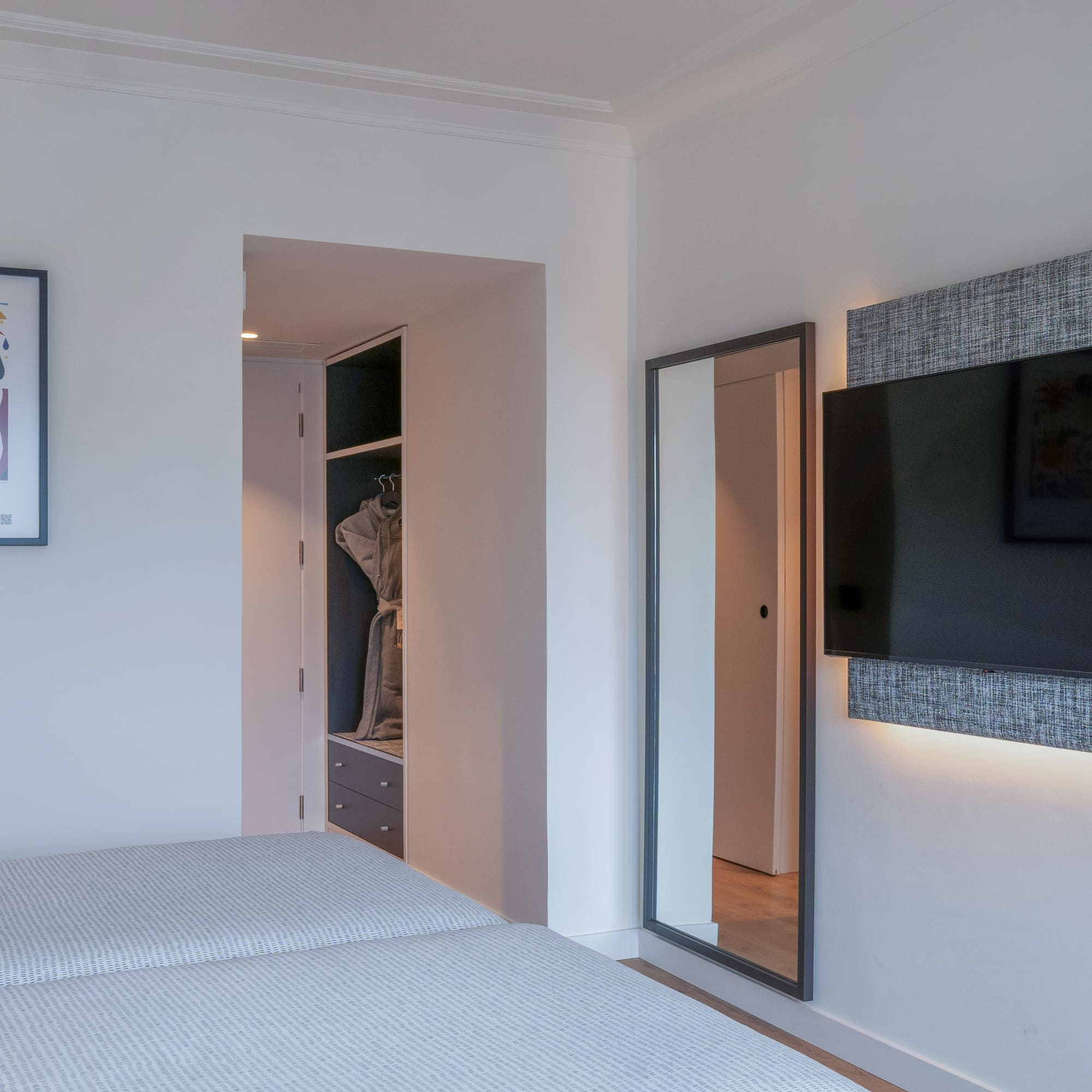 Dormitorio de hotel moderno con camas, TV retroiluminada, espejo y armario.