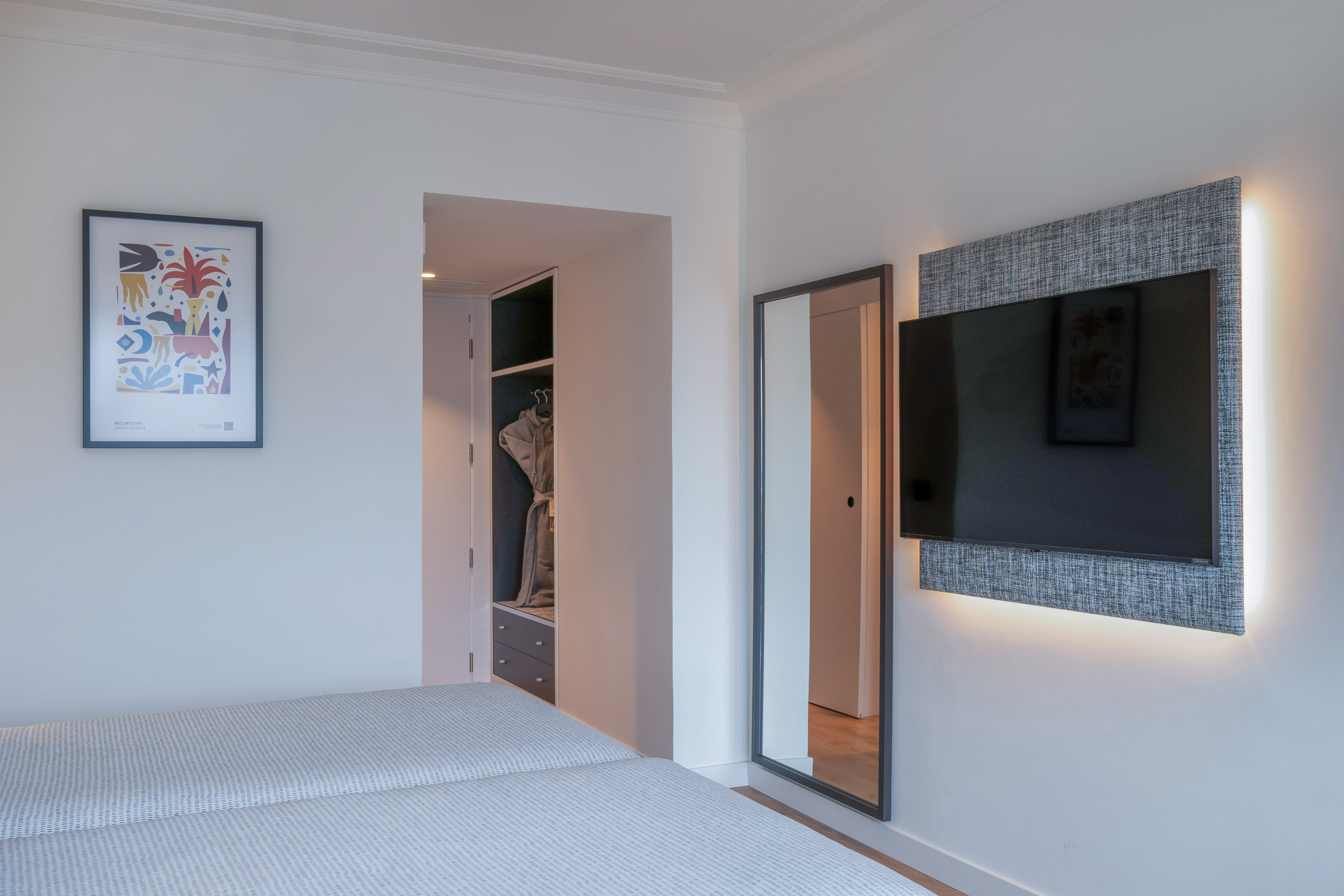 Dormitorio de hotel moderno con camas, TV retroiluminada, espejo y armario.