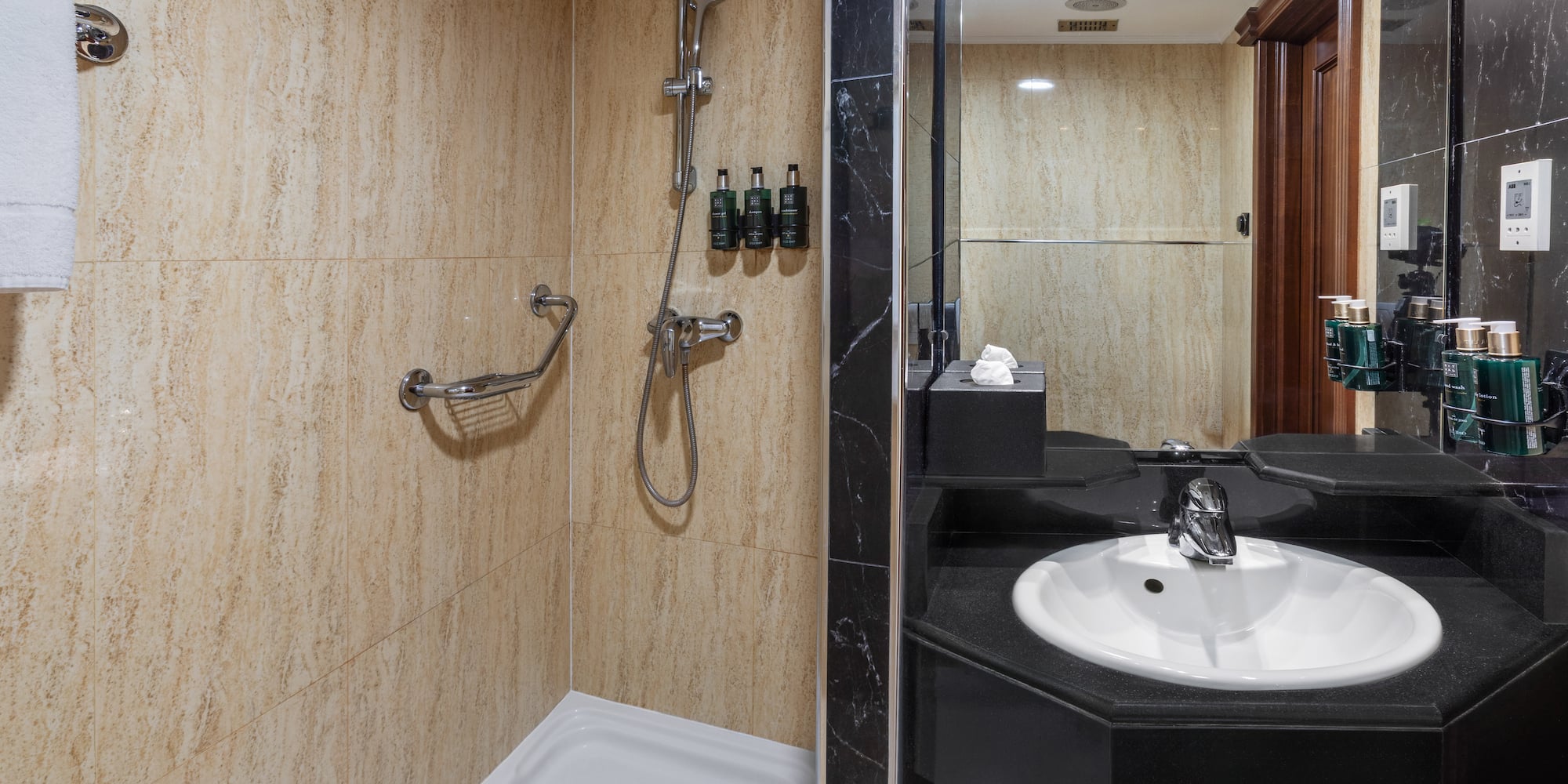 Bathroom with beige tiled shower, grab bar, and black sink vanity with mirror.