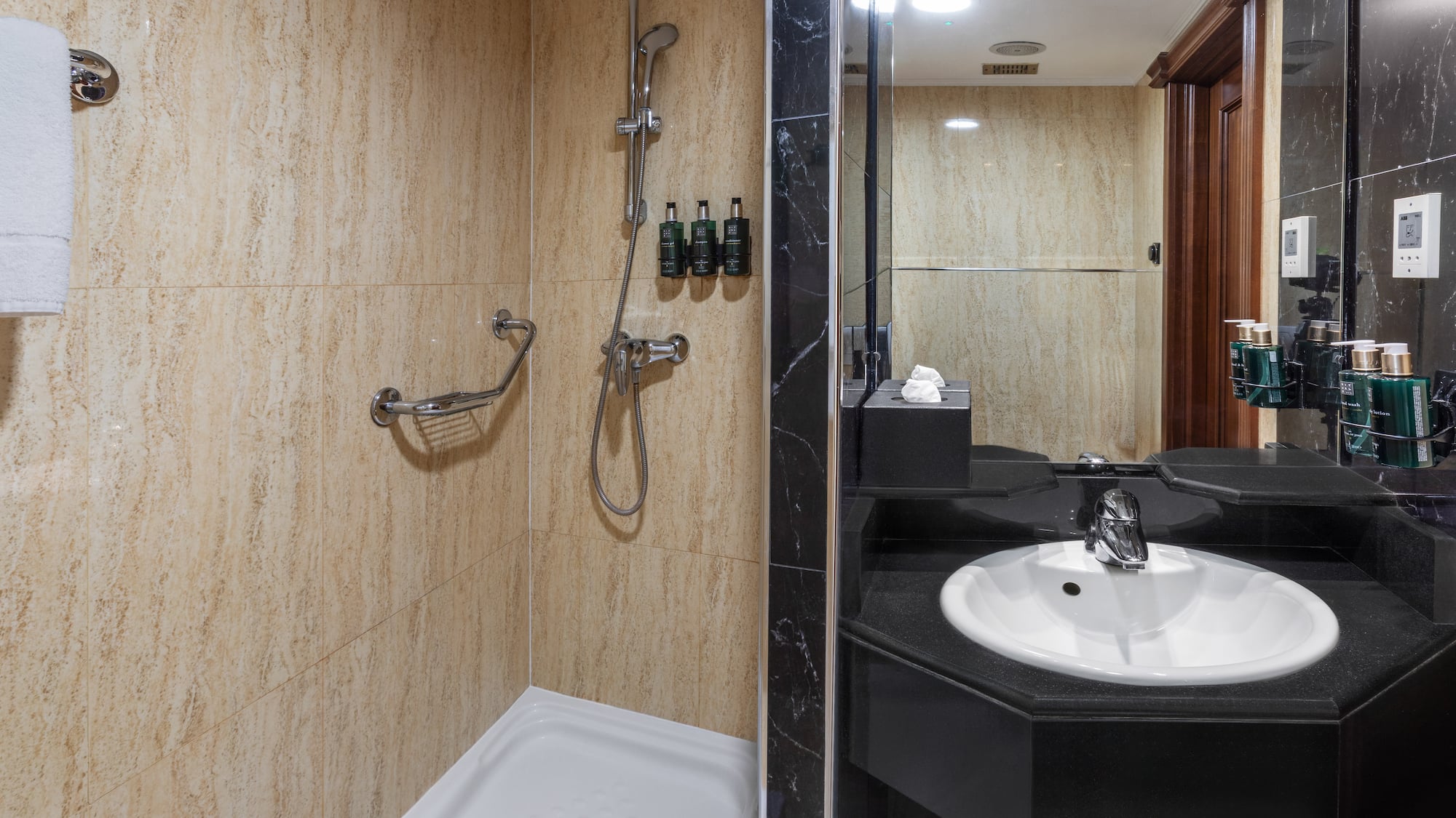 Bathroom with beige tiled shower, grab bar, and black sink vanity with mirror.