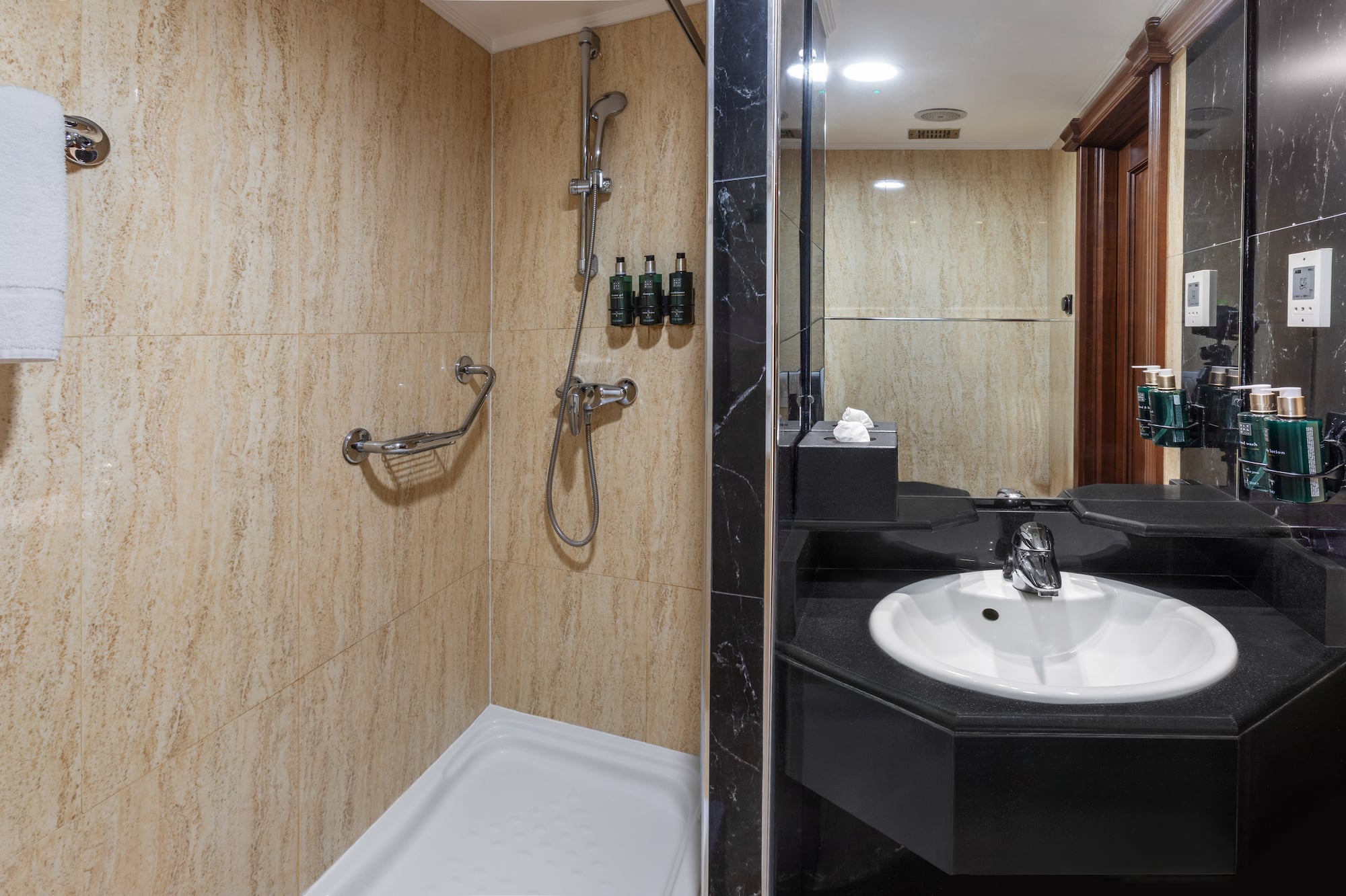 Bathroom with beige tiled shower, grab bar, and black sink vanity with mirror.
