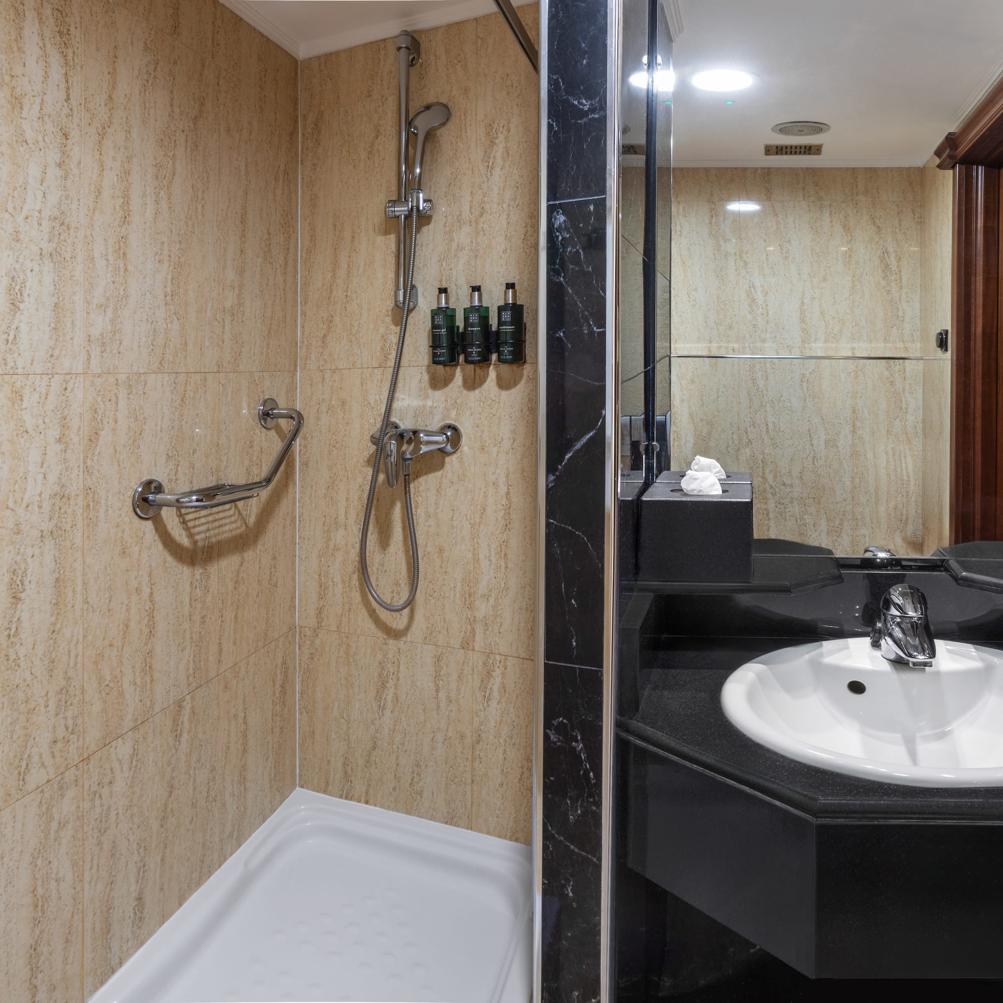 Bathroom with beige tiled shower, grab bar, and black sink vanity with mirror.