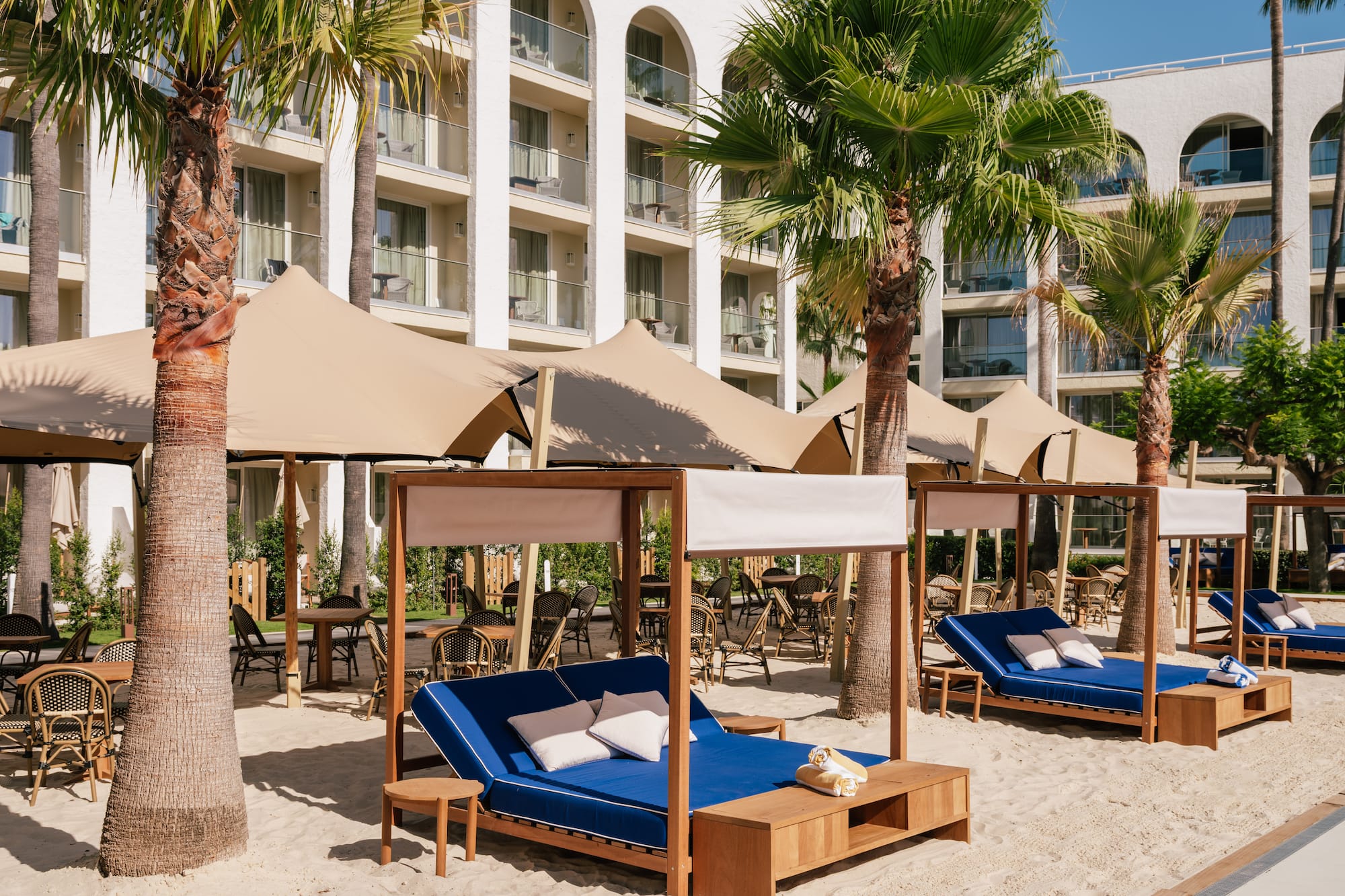 Luxury resort with palm trees, sandy beach lounge, cabanas, and blue daybeds.