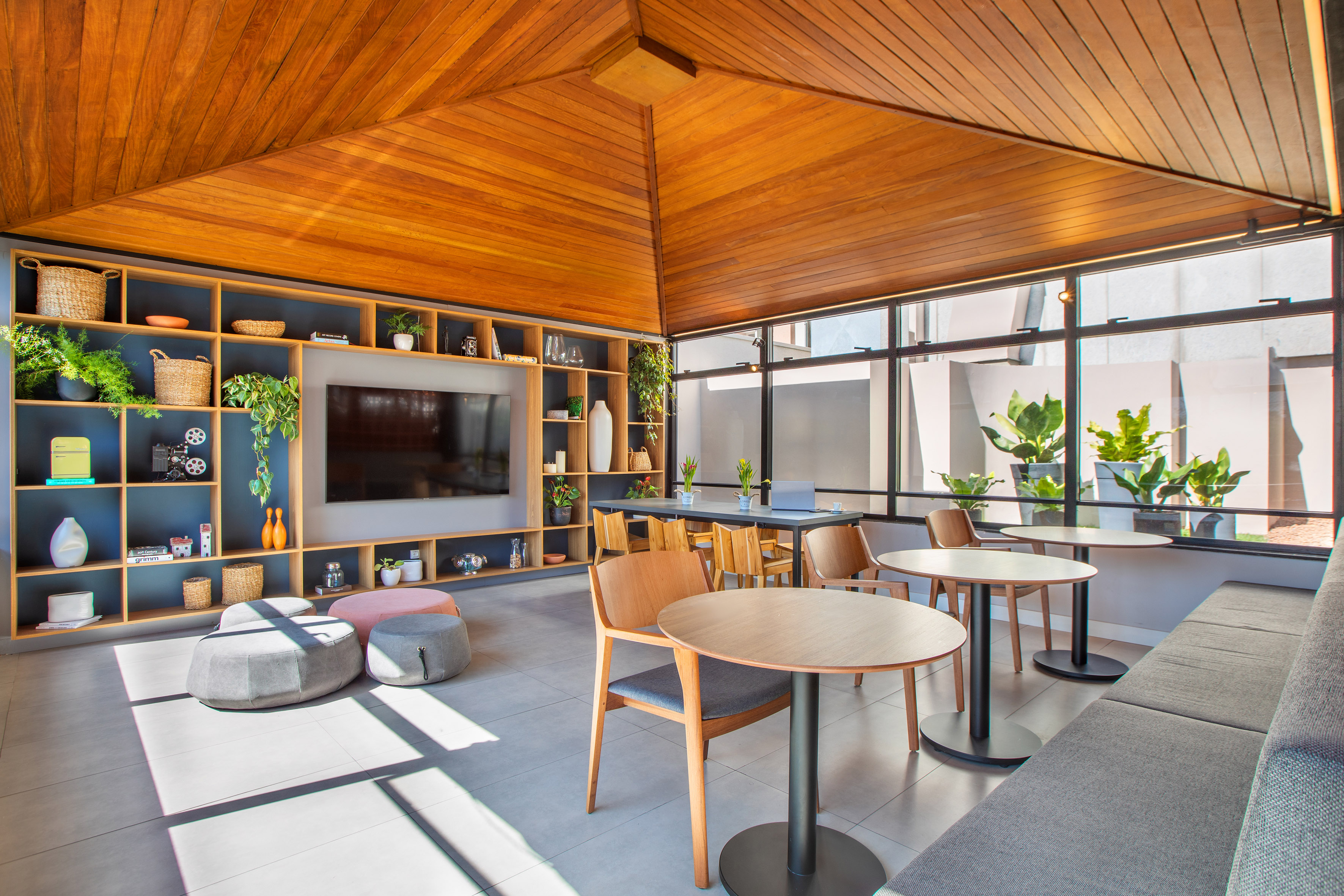 Contemporary communal lounge with wood ceiling, built-in TV shelves, and diverse seating.