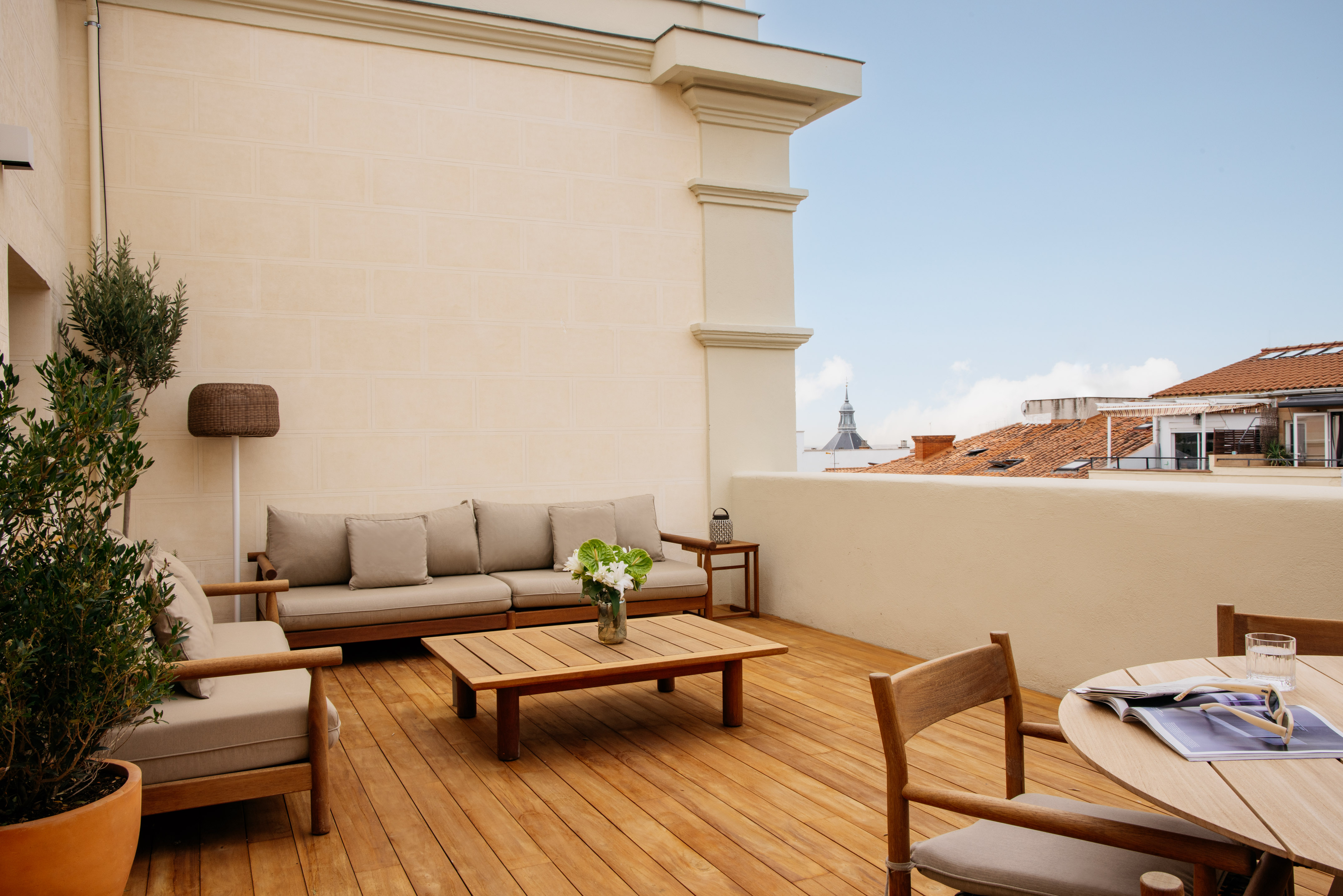 Rooftop patio with wooden deck, outdoor sofa, tables, and city view.