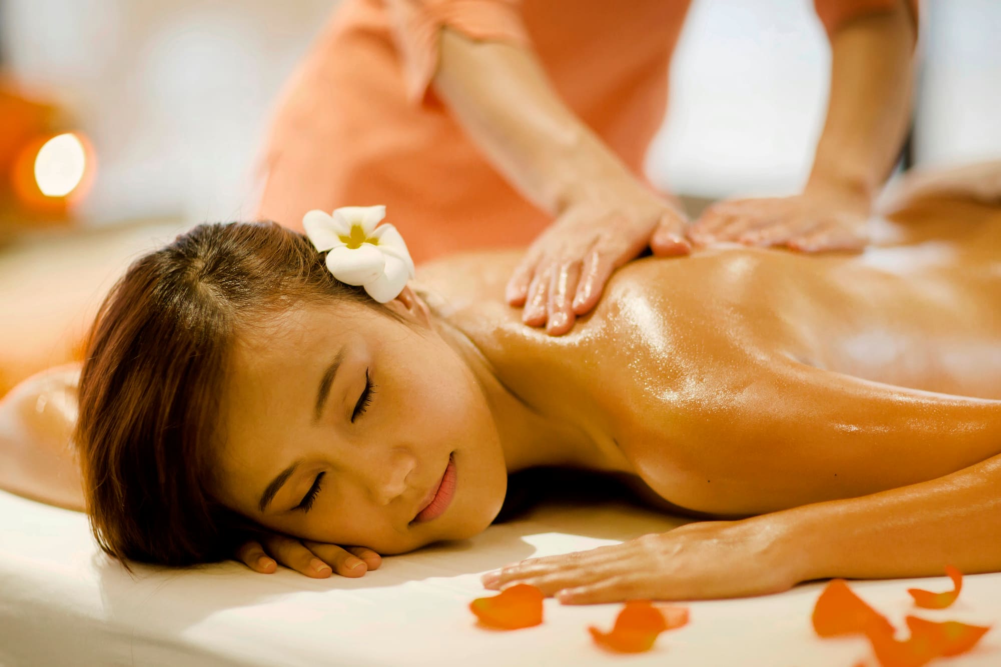 Woman with flower in hair receiving relaxing back oil massage at spa.