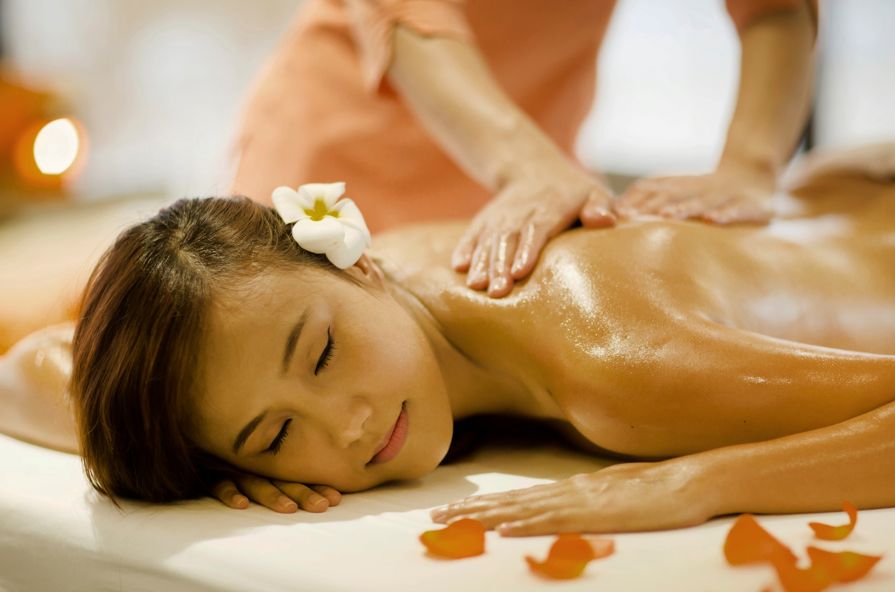 Woman with flower in hair receiving relaxing back oil massage at spa.