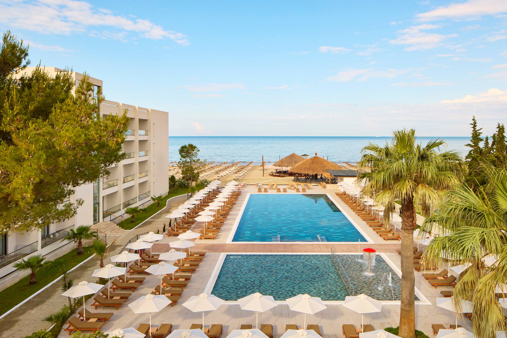 Beachfront hotel resort with swimming pools, sunbeds, palm trees, and ocean.