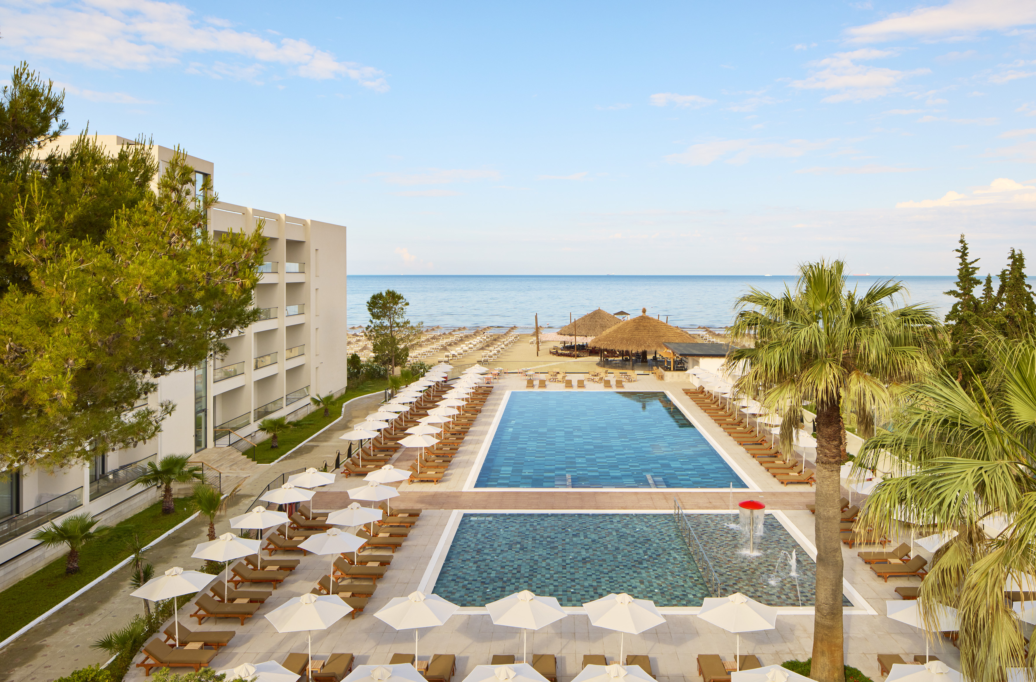 Beachfront hotel resort with swimming pools, sunbeds, palm trees, and ocean.