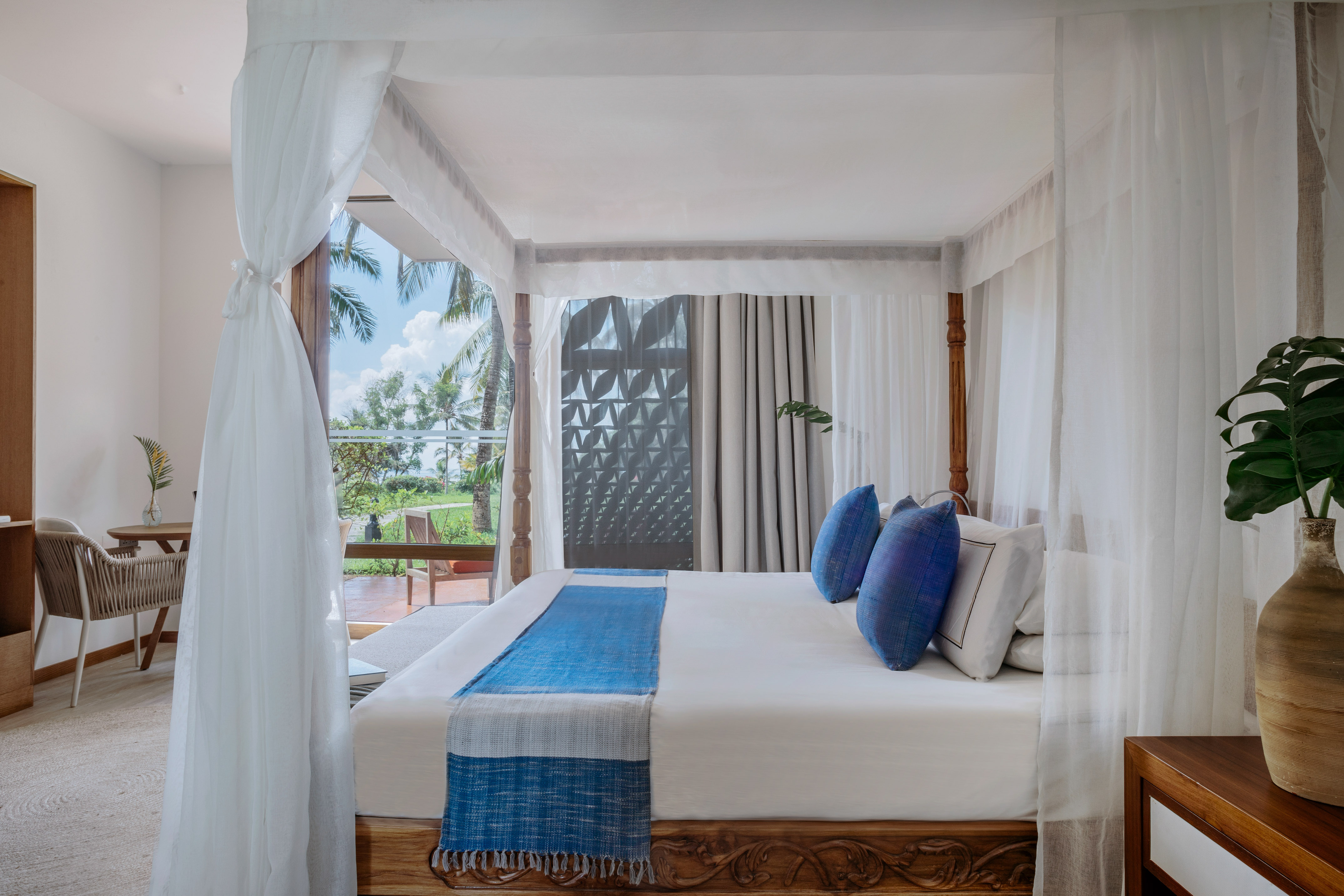 Luxury tropical bedroom with four-poster canopy bed and stunning palm tree view.