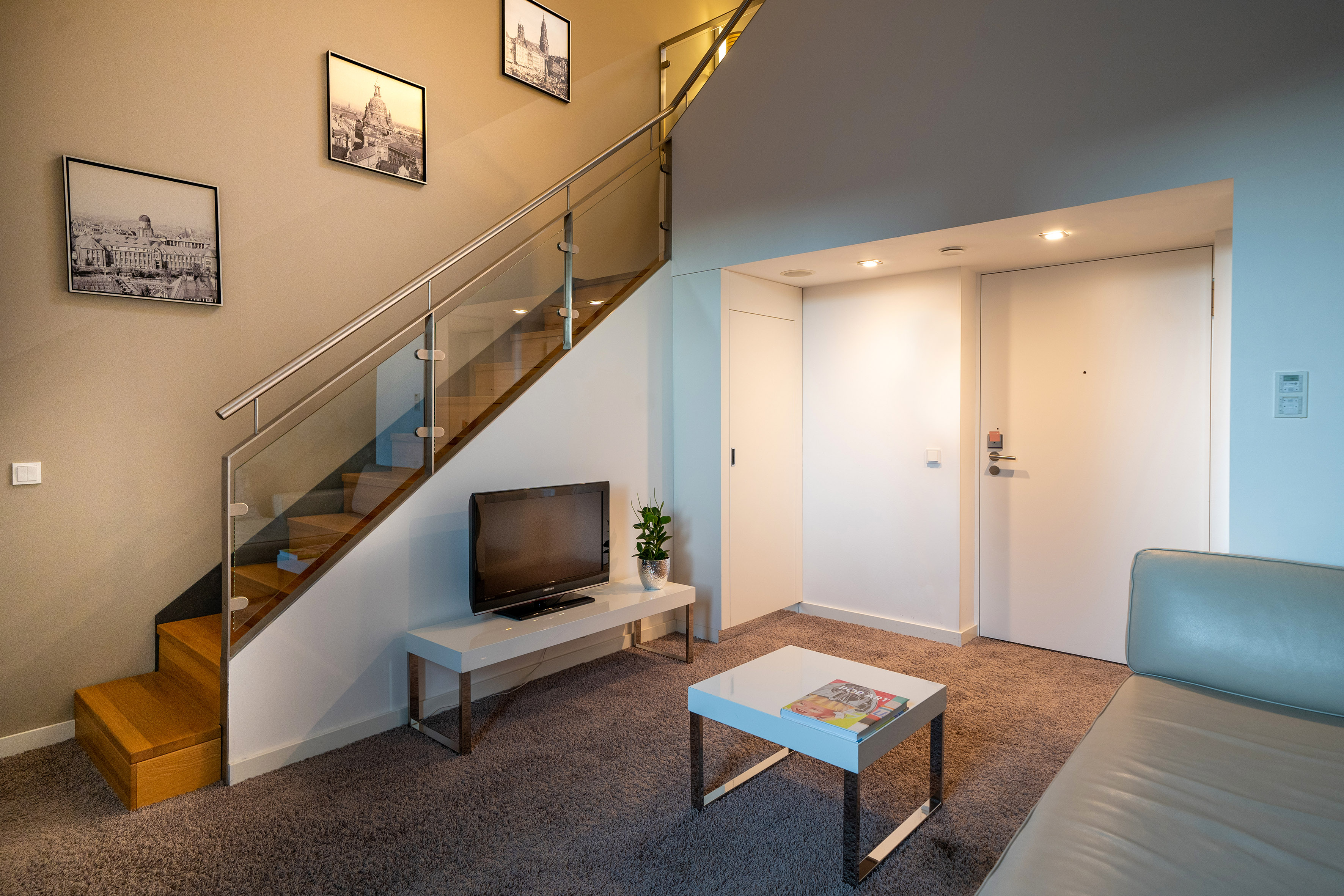Modern apartment living room with sleek glass staircase and TV area.
