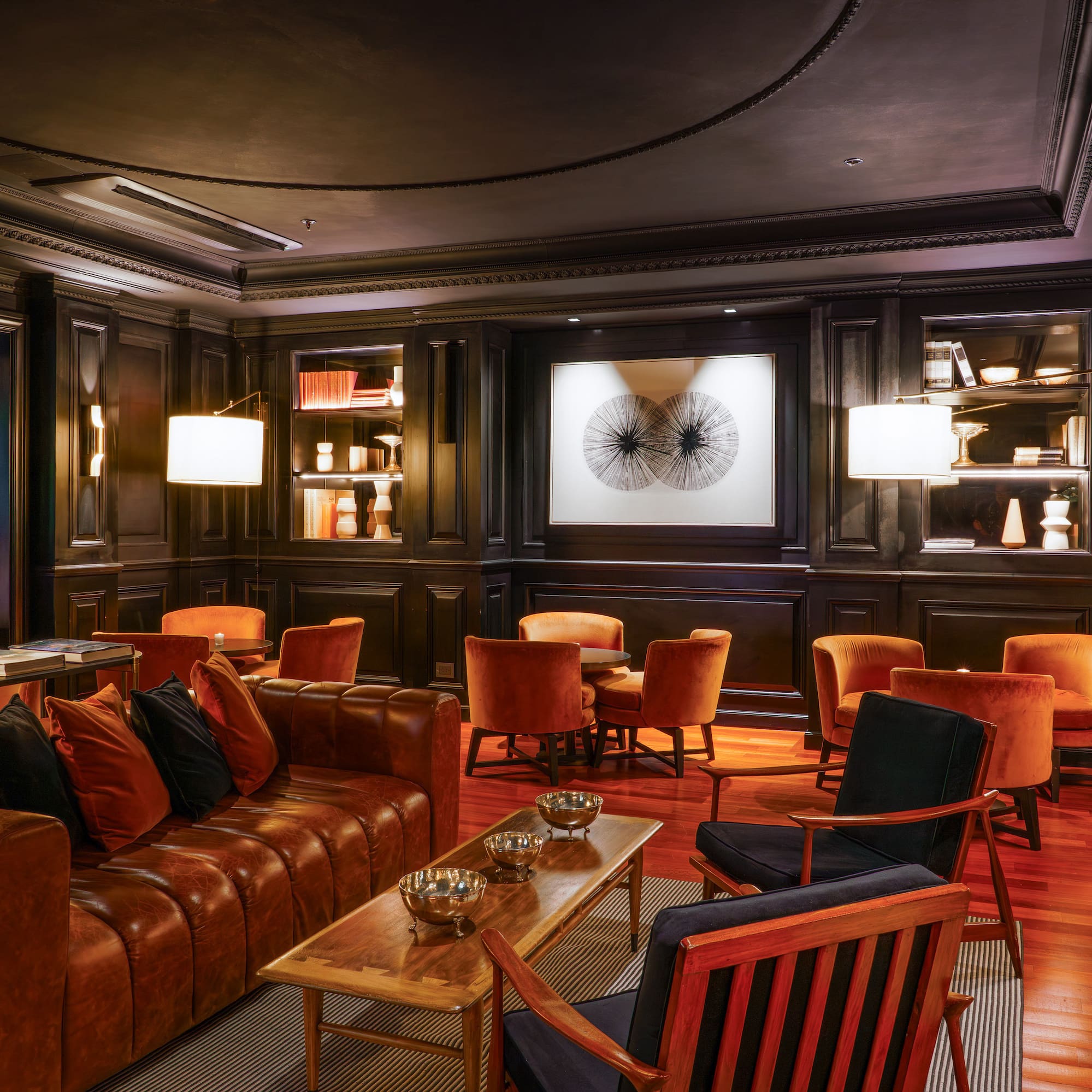 Elegant hotel lounge interior with dark wood paneling, leather sofa, and orange chairs.