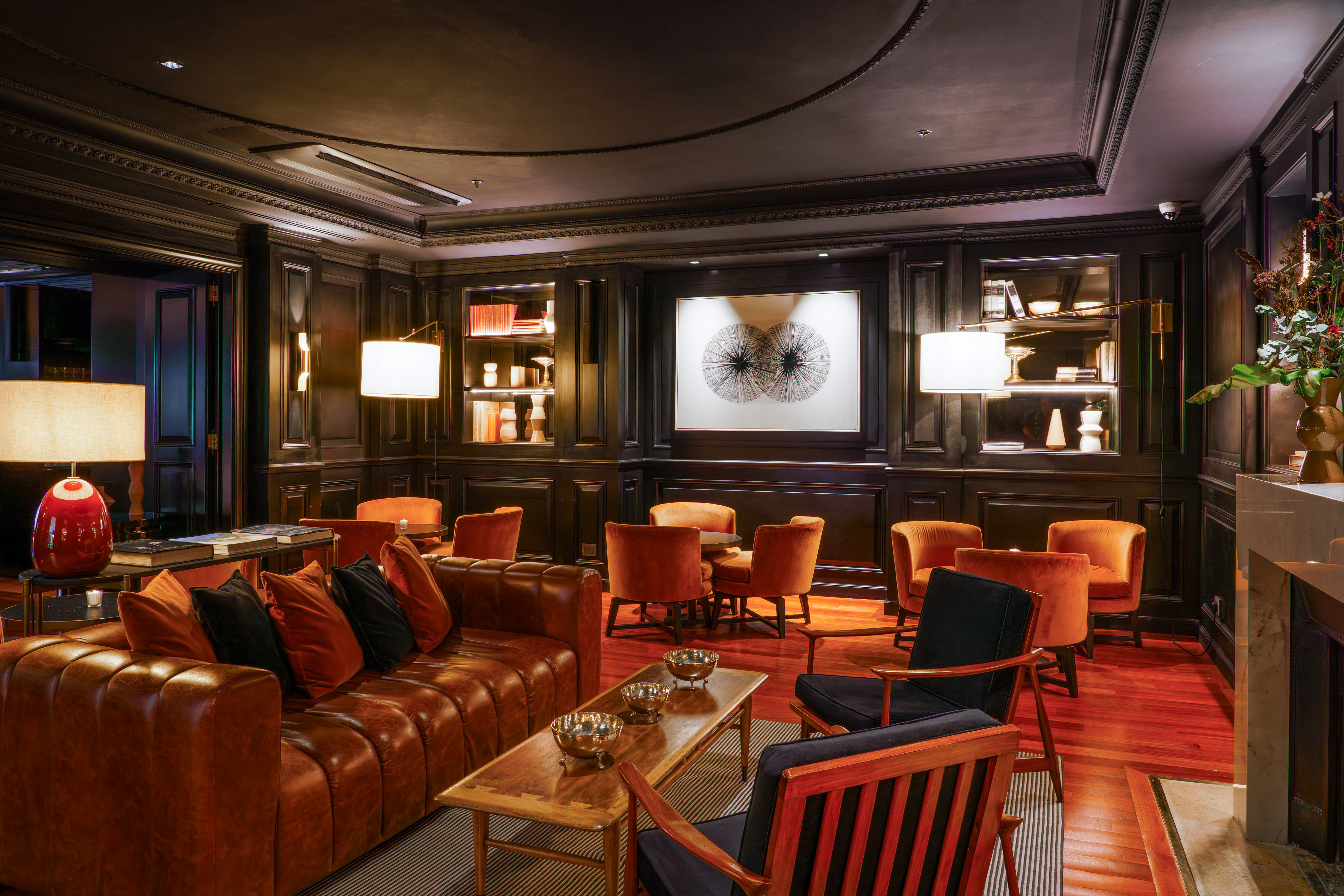 Elegant hotel lounge interior with dark wood paneling, leather sofa, and orange chairs.