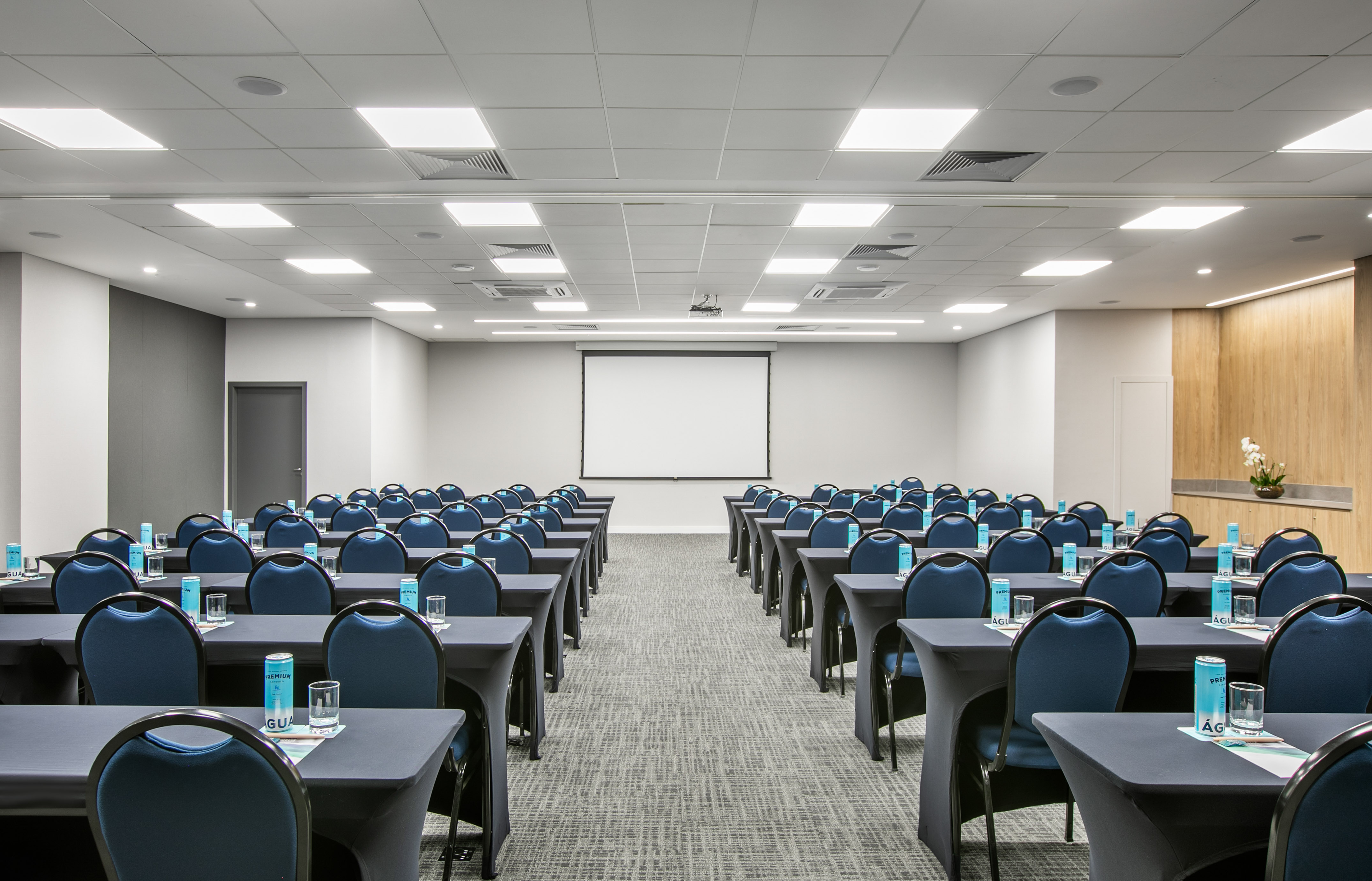 Large modern conference room with blue chairs, tables, and projector screen.