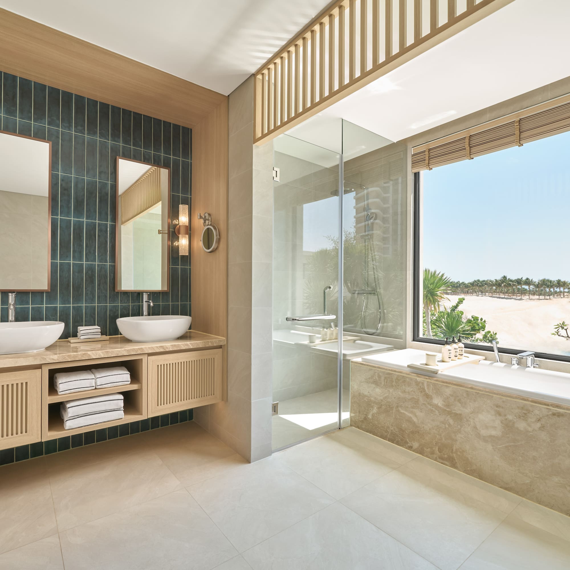 Modern bathroom with dual sinks, bathtub, glass shower, and beach view.