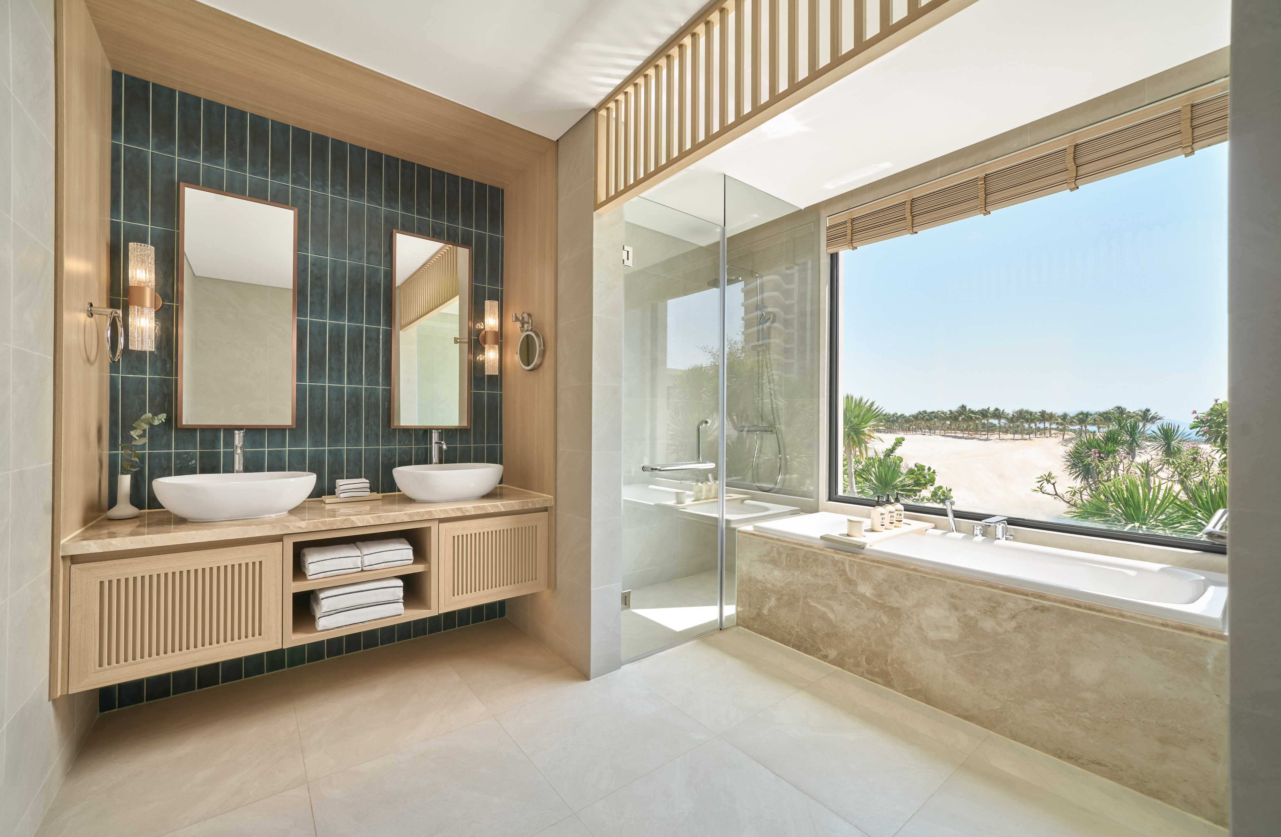 Modern bathroom with dual sinks, bathtub, glass shower, and beach view.