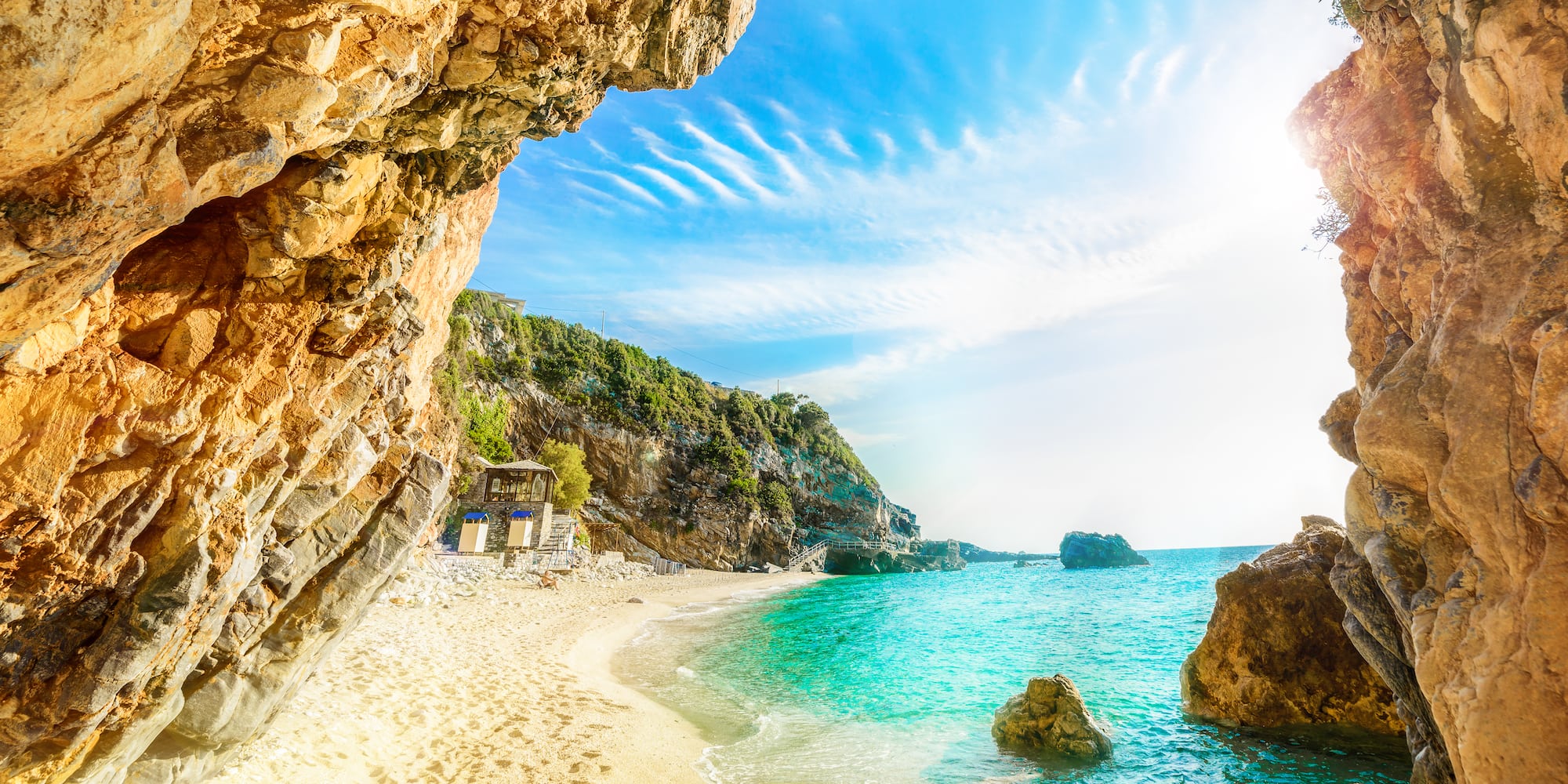 Cala con playa de arena, aguas turquesas, acantilados rocosos y sol.