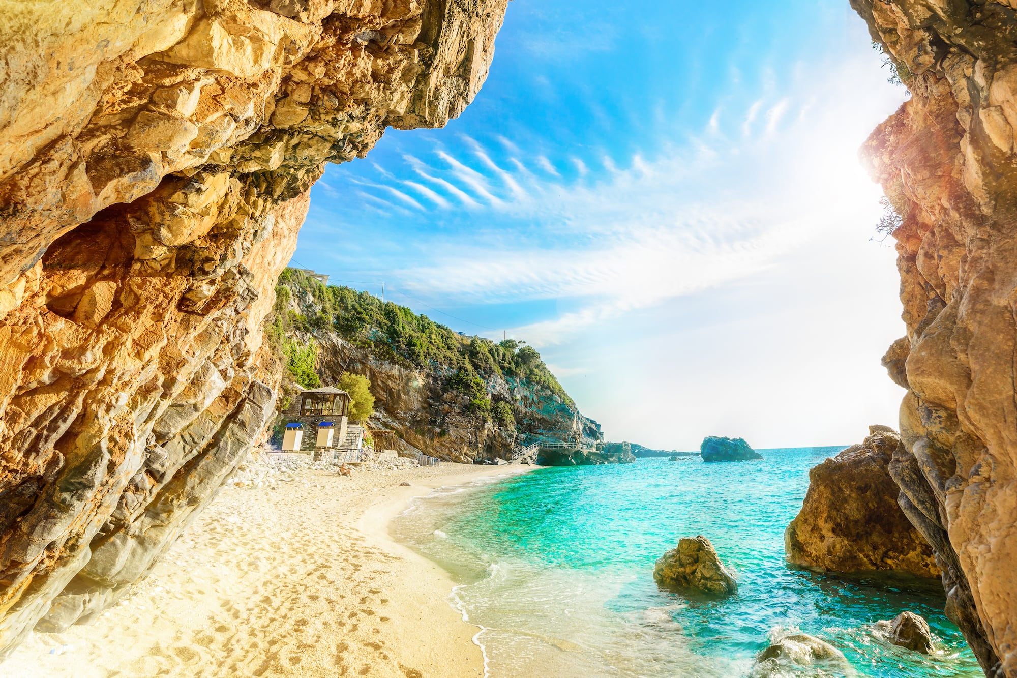 Secluded beach cove with turquoise water, golden sand, and sunlit rock cliffs.