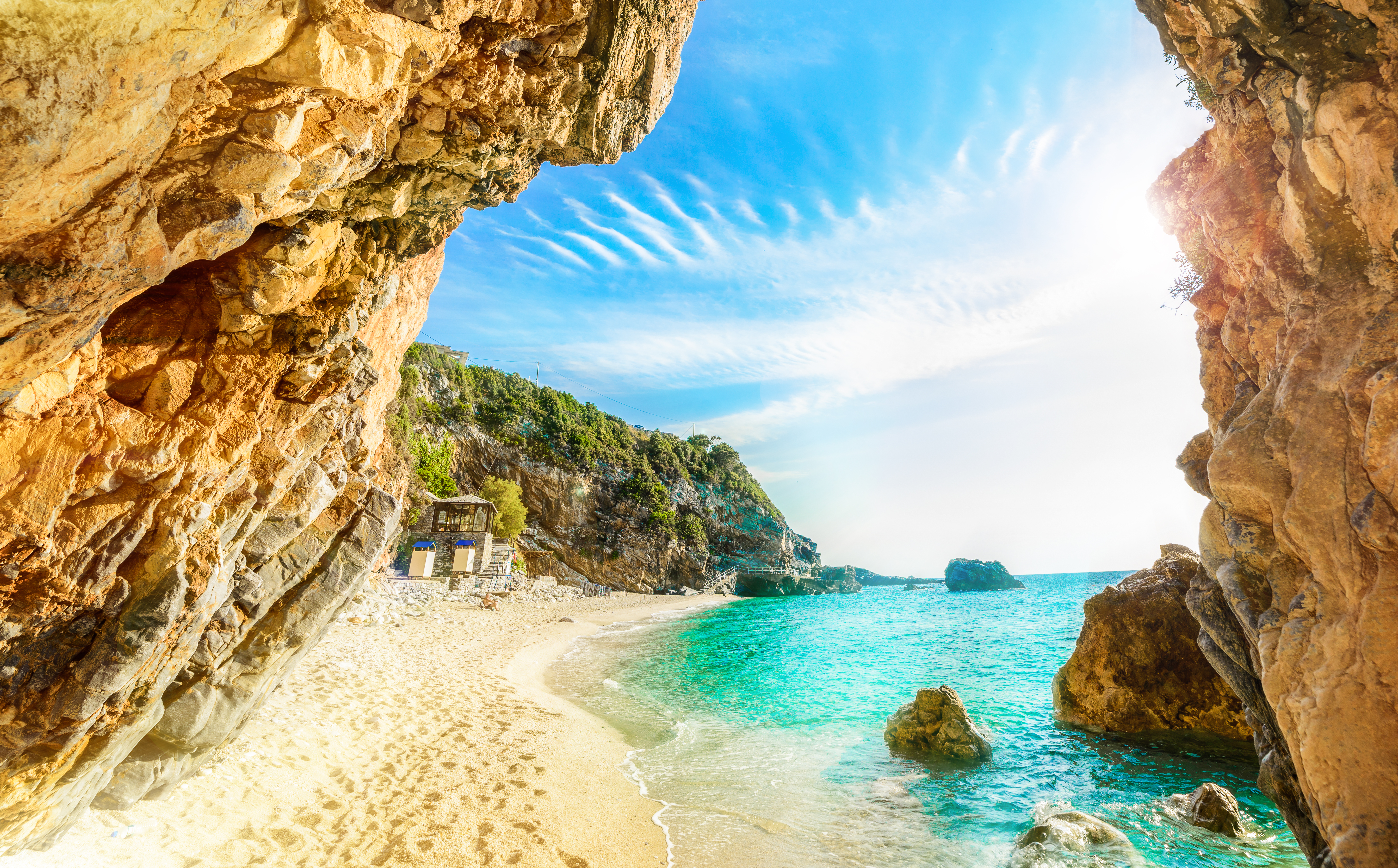 Secluded beach cove with turquoise water, golden sand, and sunlit rock cliffs.