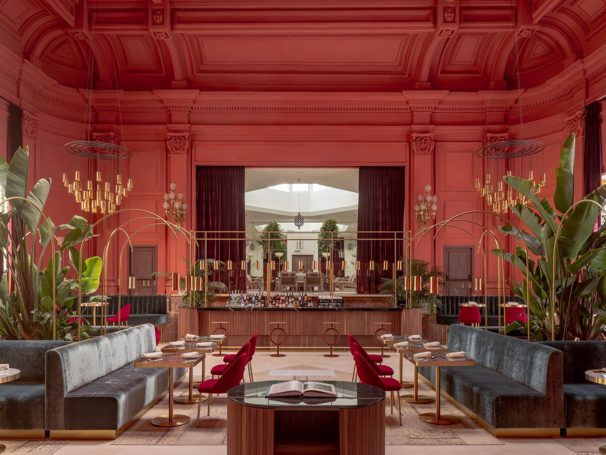 Chic coral restaurant interior with velvet seating, gold bar, and lush plants.