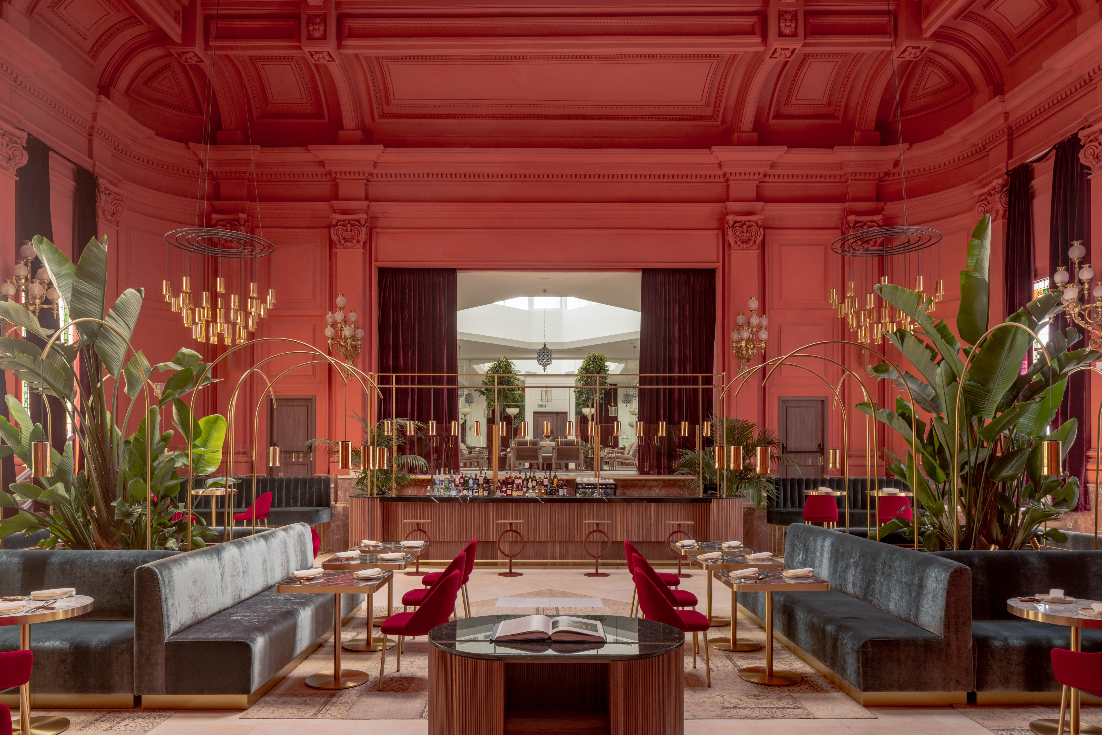 Chic coral restaurant interior with velvet seating, gold bar, and lush plants.