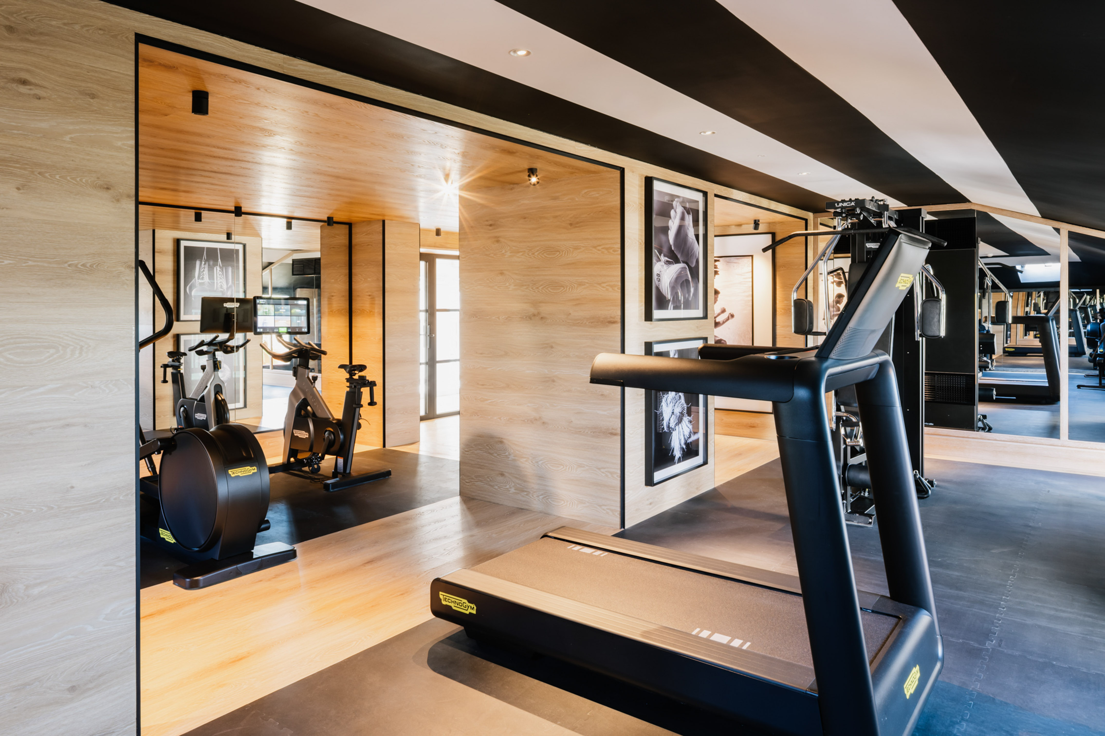 Modern home gym with treadmill, exercise bikes, wood walls, and striped ceiling.