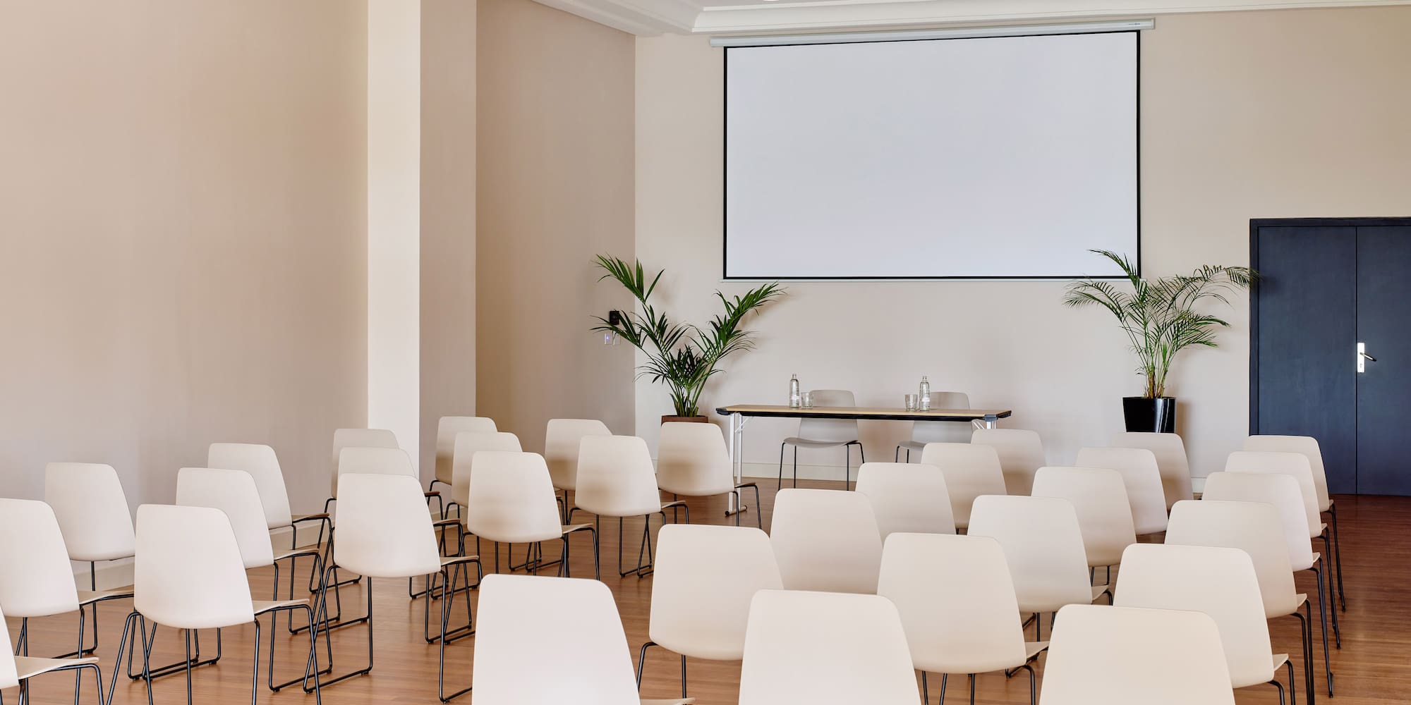 Empty modern conference room with projection screen and rows of chairs.