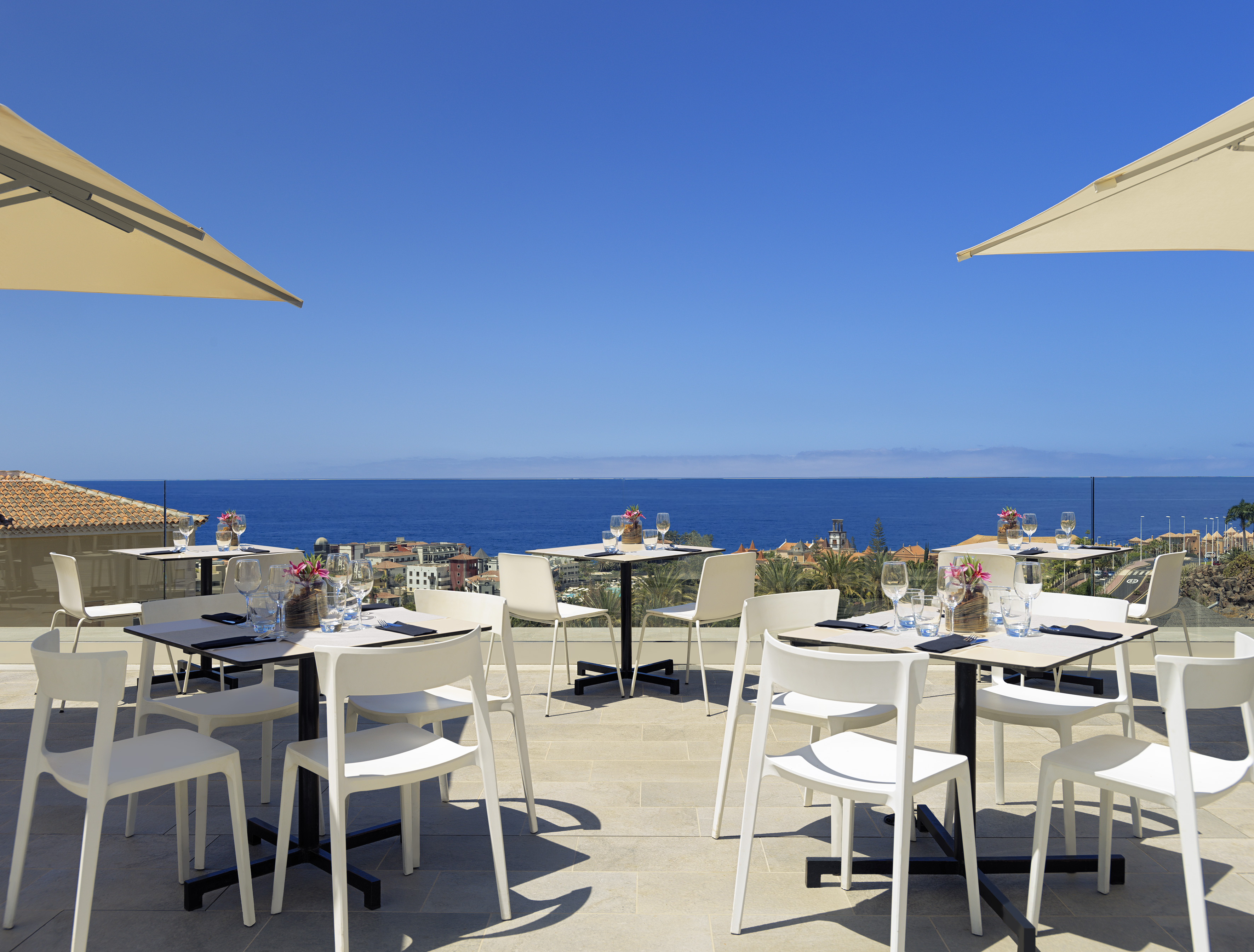 Sunny patio restaurant with ocean view, white dining tables and umbrellas.