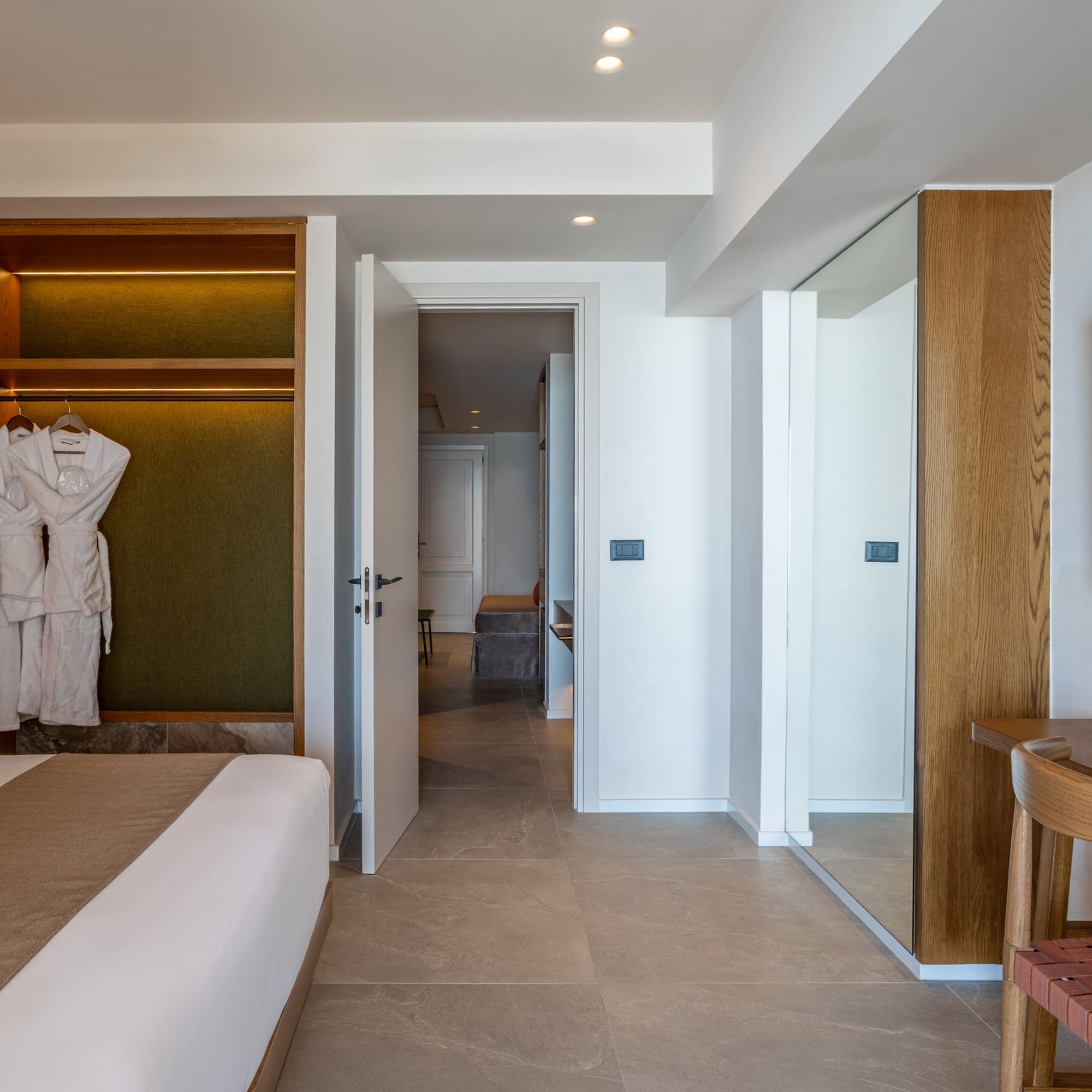 Modern hotel bedroom with open closet, bathrobes, large bed, and wall-mounted TV.