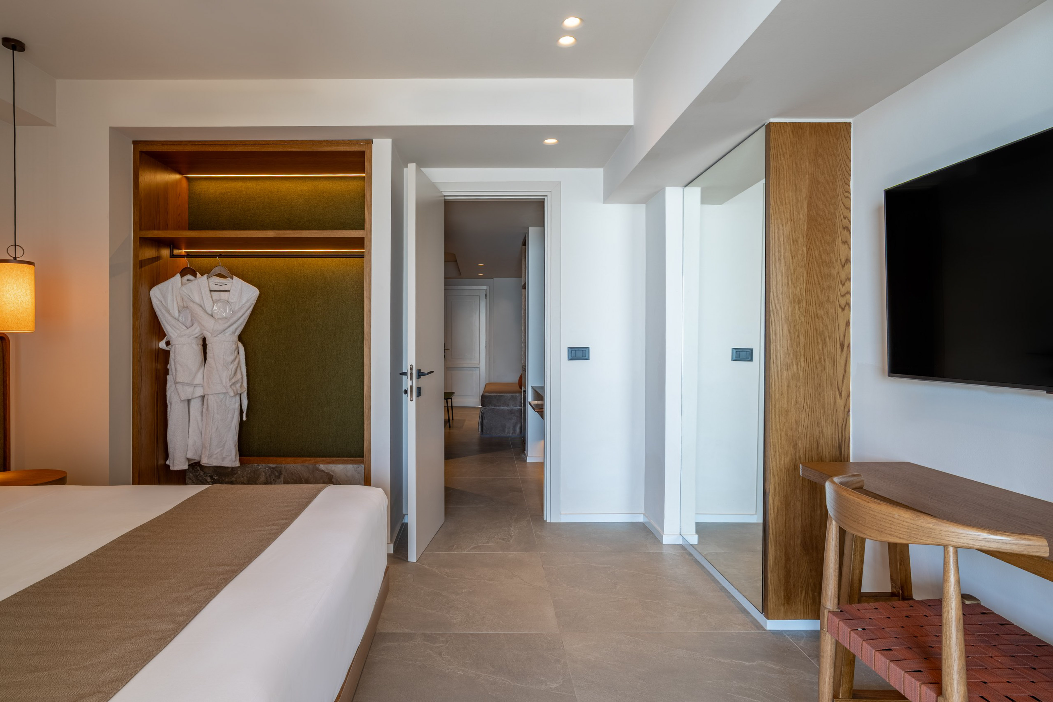 Modern hotel bedroom with open closet, bathrobes, large bed, and wall-mounted TV.