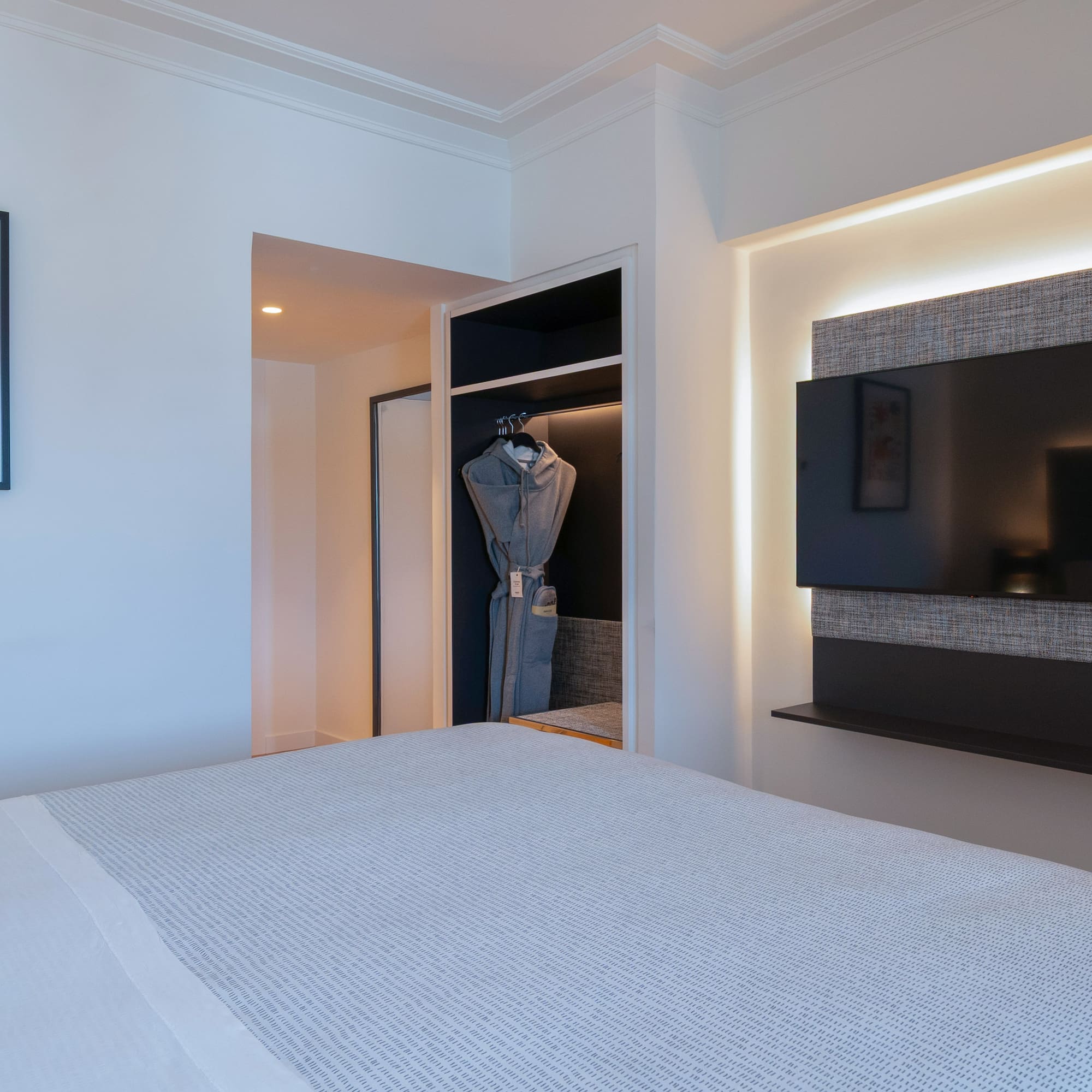 Habitación moderna de hotel: cama, TV retroiluminada, armario y cuadro abstracto.