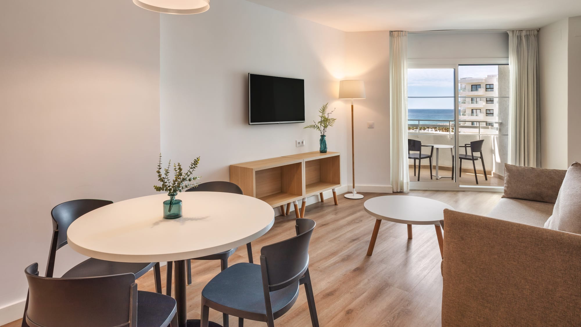 Modern apartment living room with dining area and ocean view balcony.
