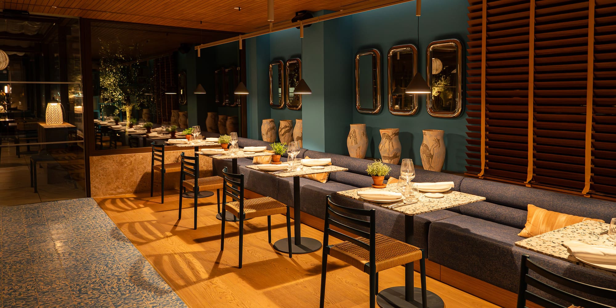 Modern restaurant interior with set tables, teal wall, and banquette seating.
