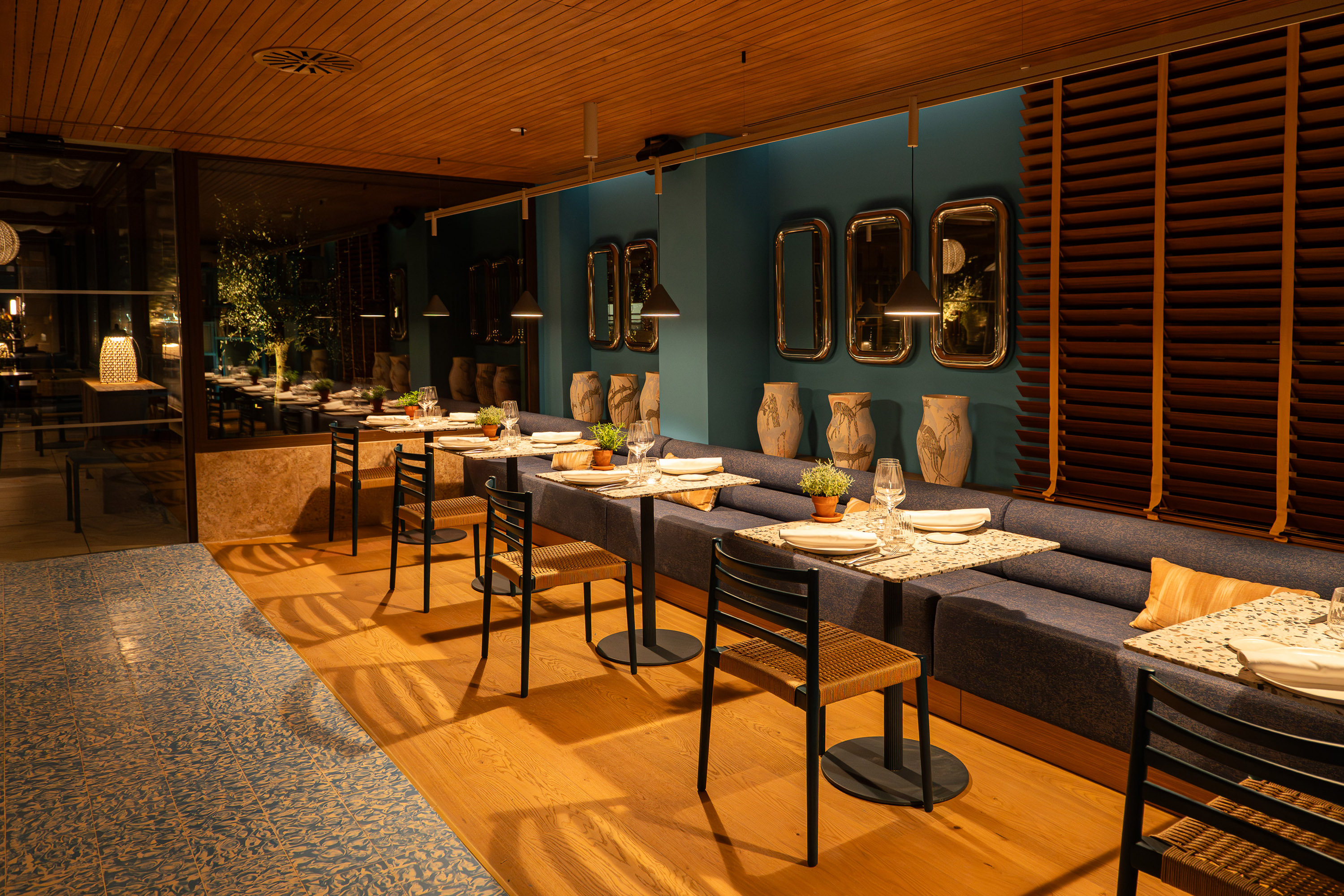 Modern restaurant interior with set tables, teal wall, and banquette seating.