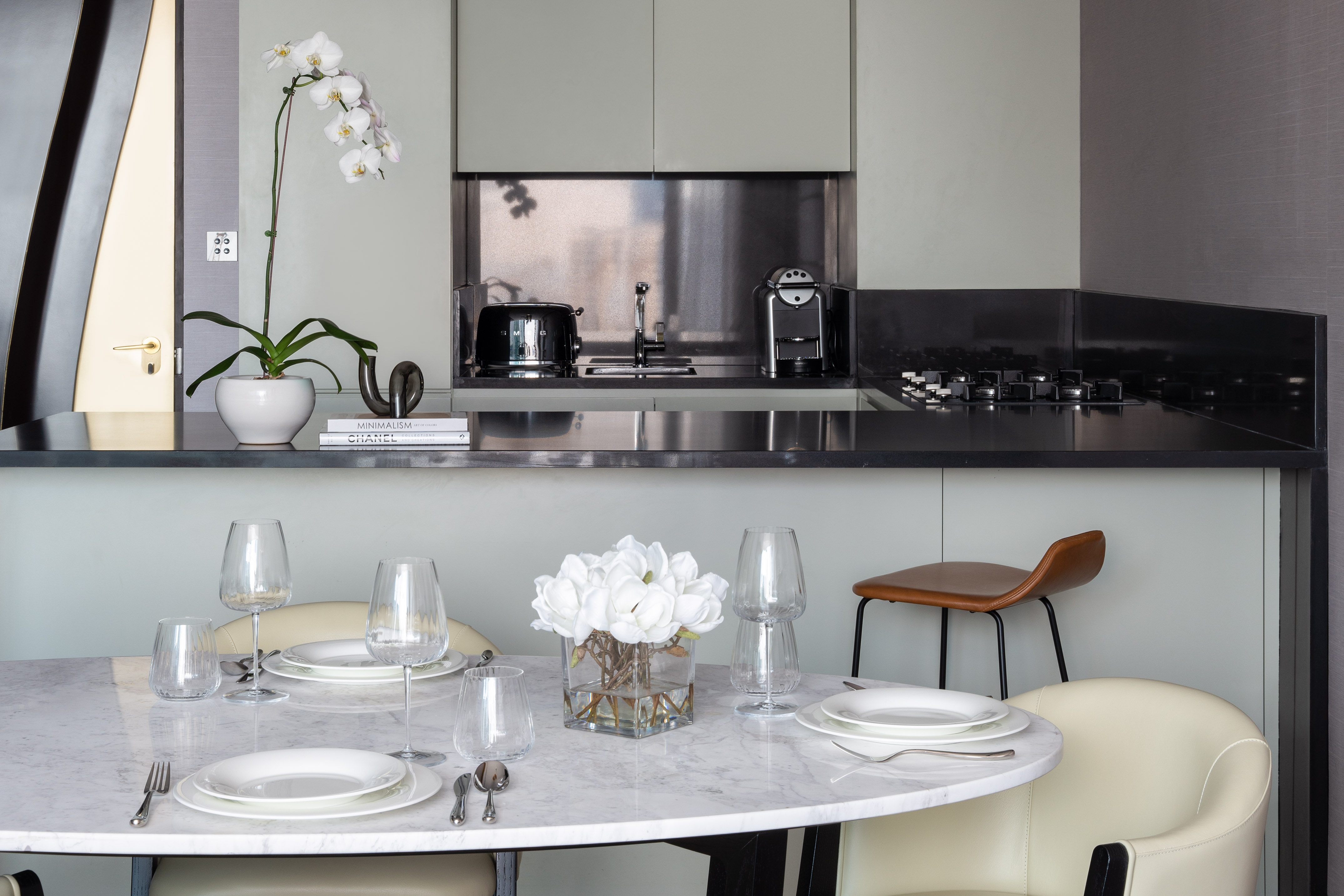 Modern kitchen dining area with marble table, white orchid, and coffee machine.