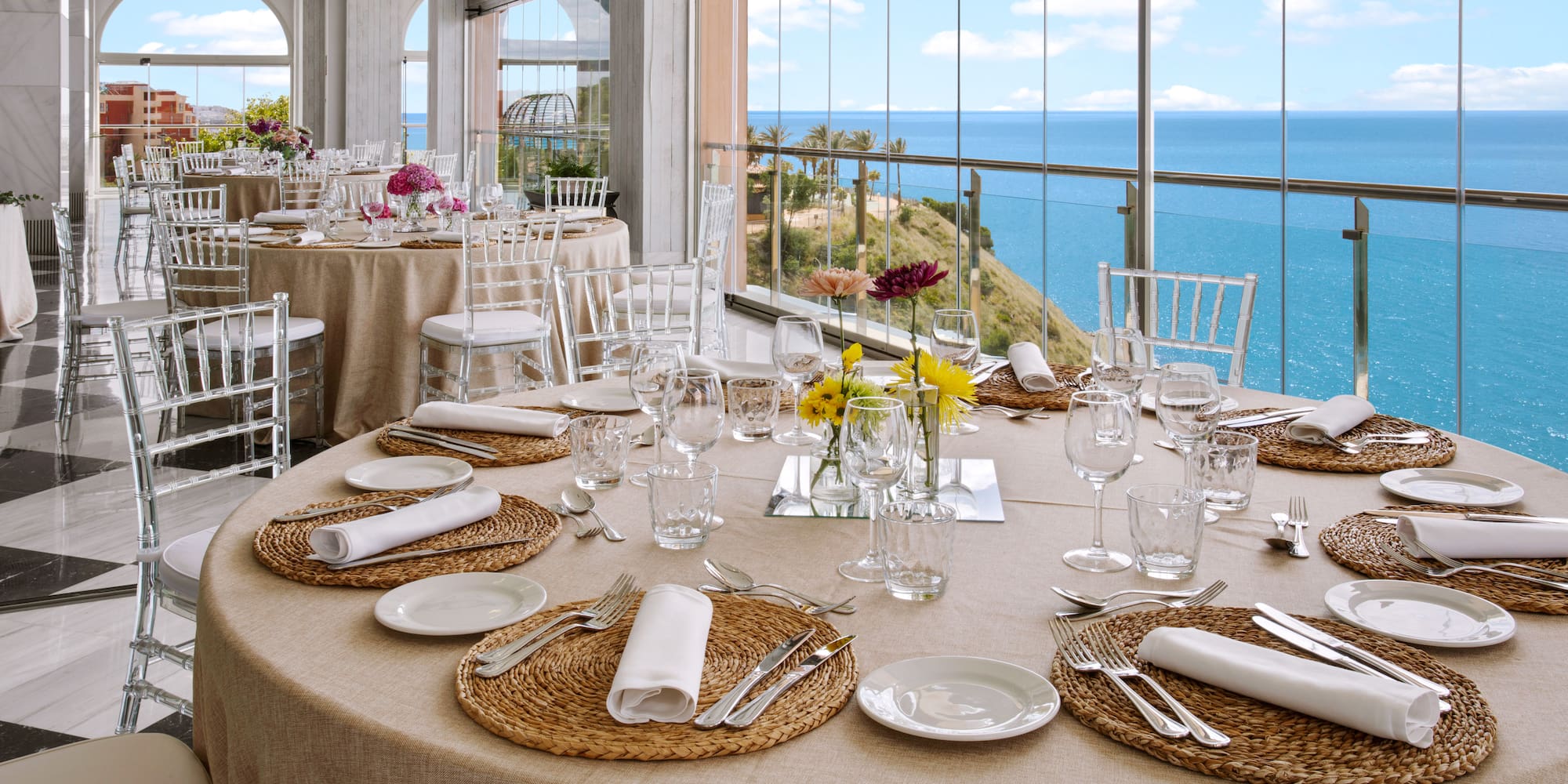 Elegant dining tables set for an event with panoramic sea views.