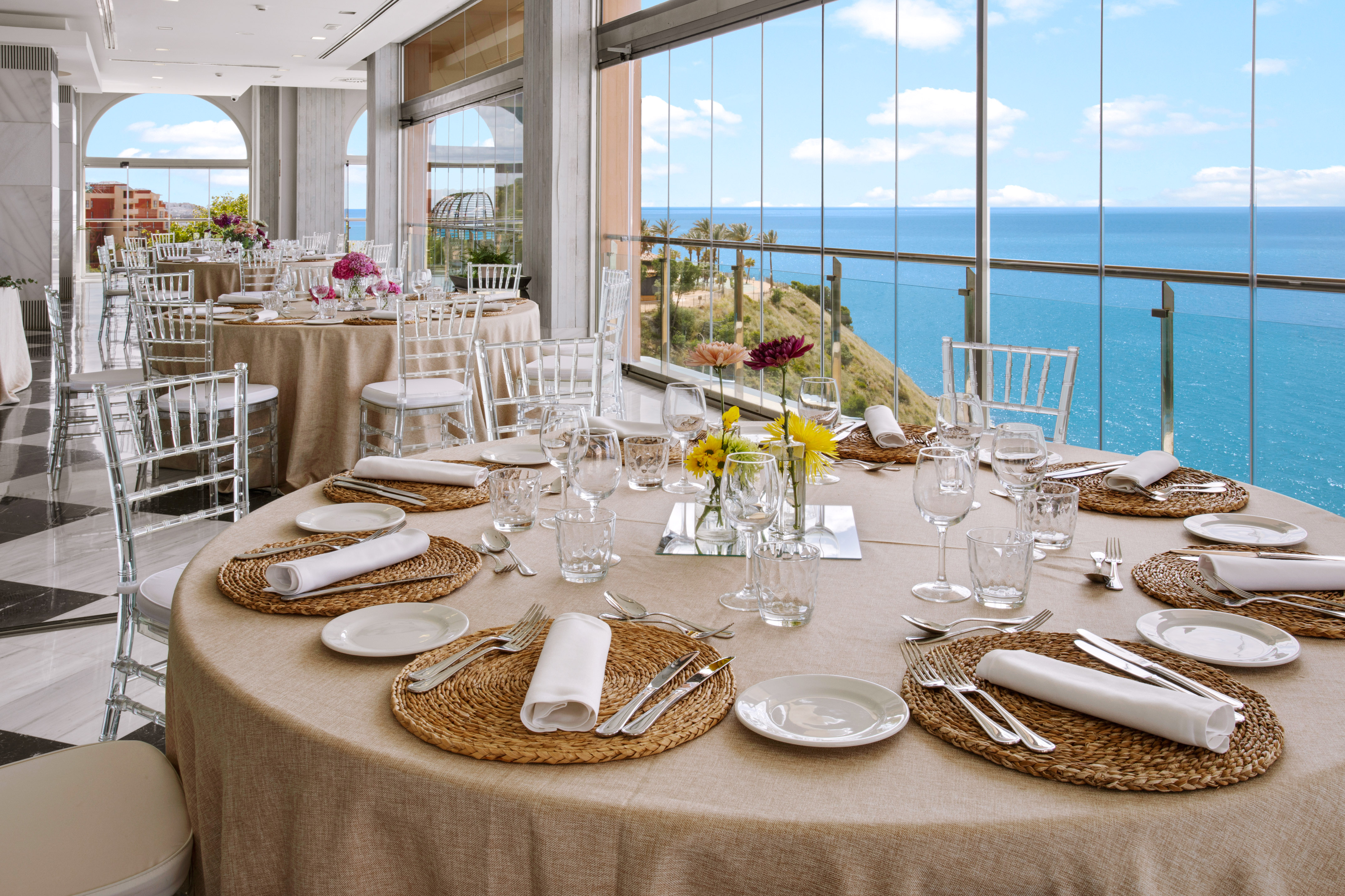 Elegant dining tables set for an event with panoramic sea views.