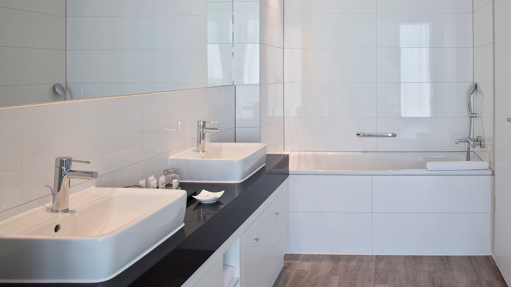Modern bathroom with double vanity, black countertop, white tiles, and bathtub.