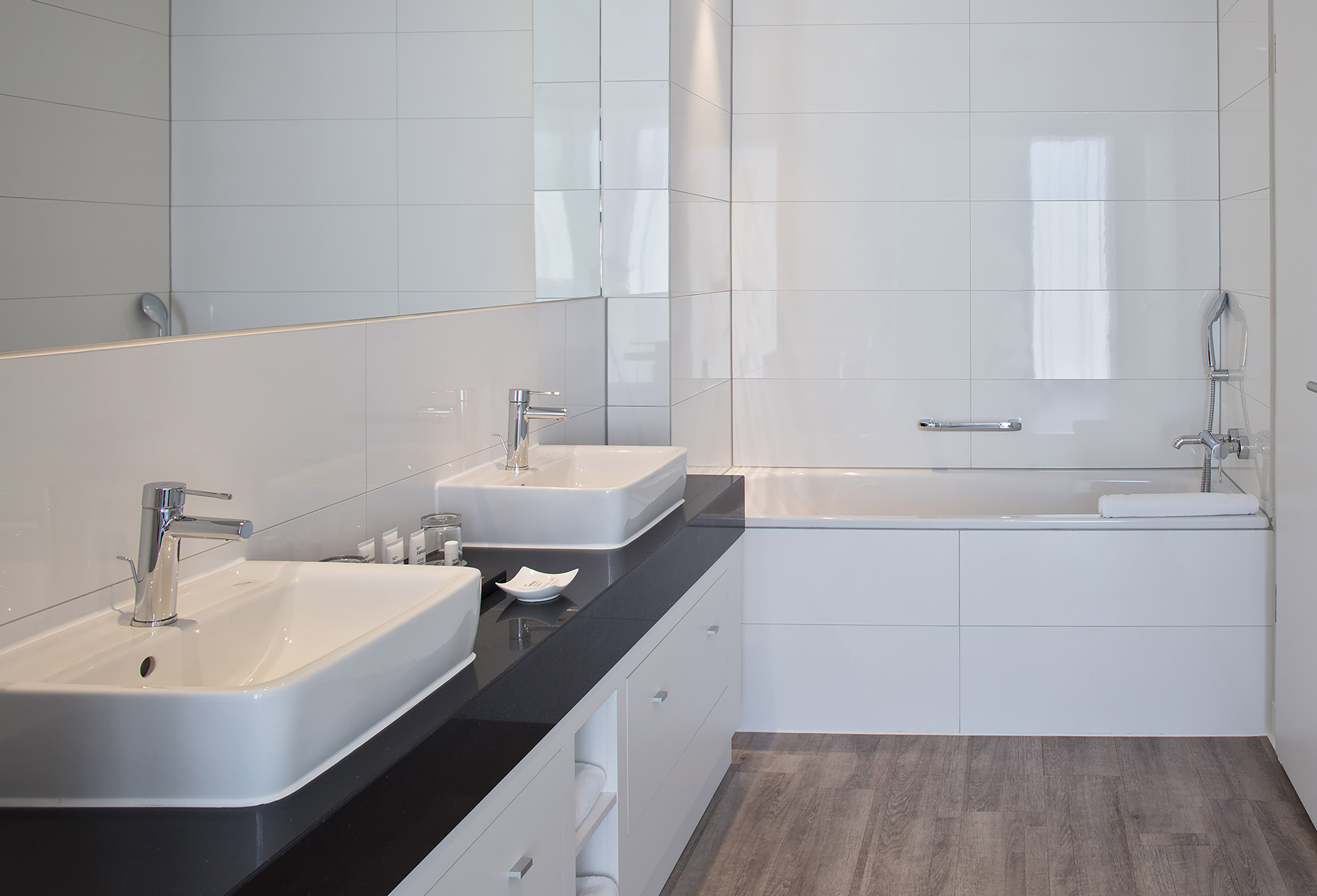 Modern bathroom with double vanity, black countertop, white tiles, and bathtub.